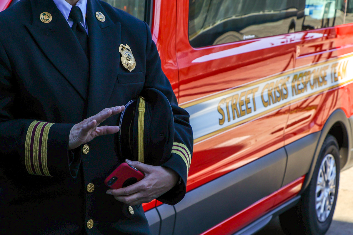 A man in a fire department uniform is seen standing near a large red van with lettering on the side reading "street crisis response team."