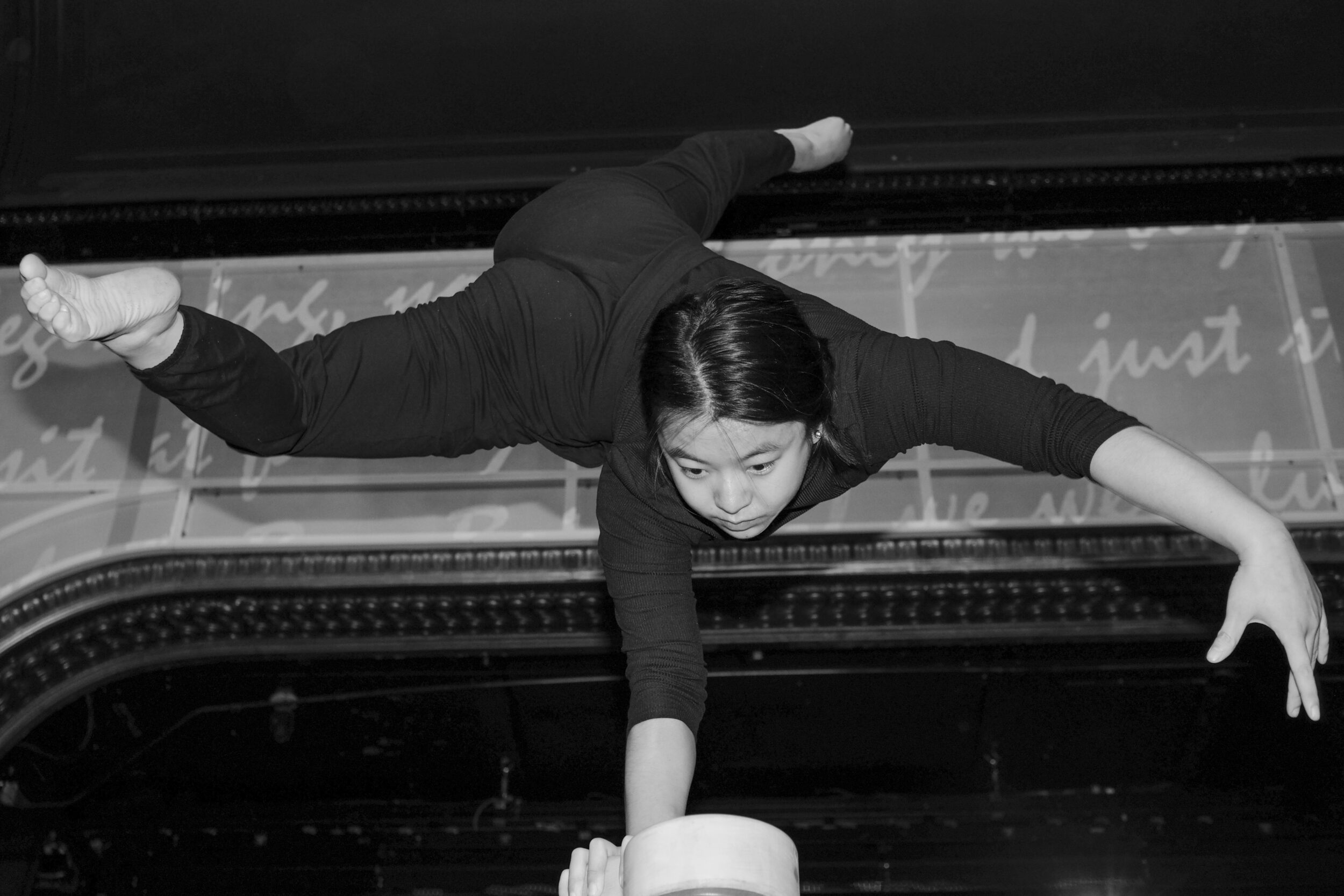 A woman on a stage in a black unitard practices a balancing act.