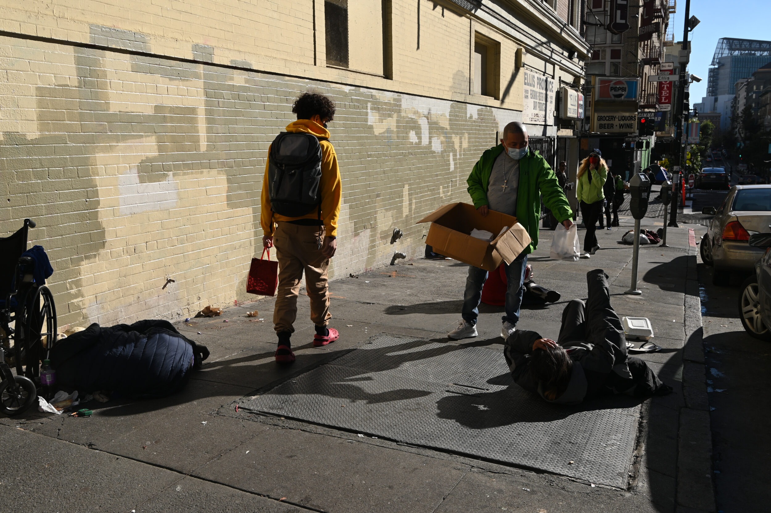 People walk past others lying on the sidewalk.