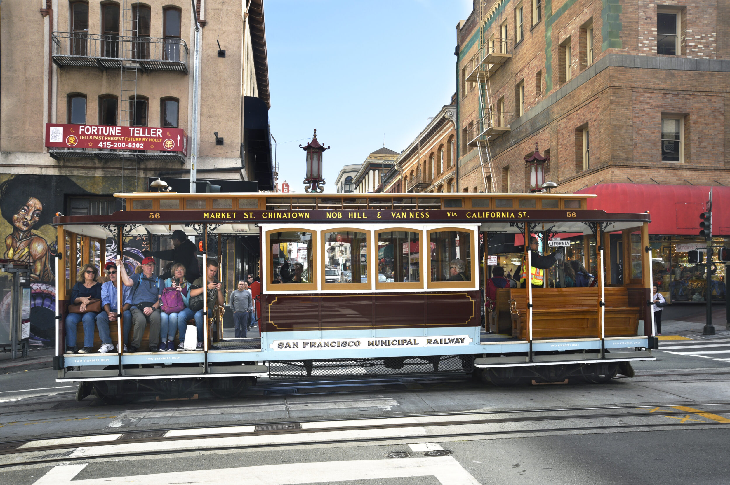 A cable car travels along tracks in San Francisco's chinatown with tourists aboard.
