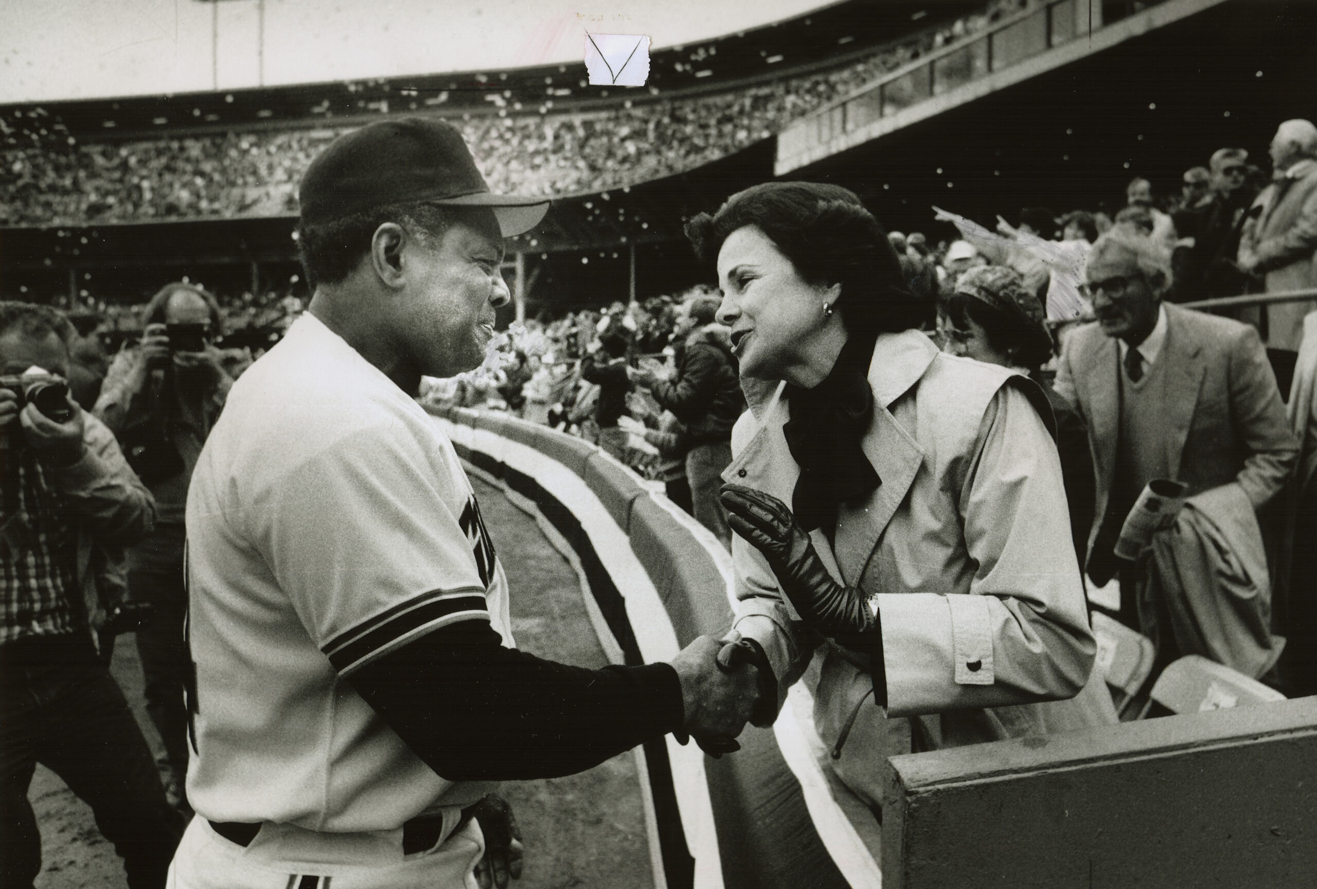 A baseball player shakes a woman's hand in a black and white photo  baseball field. 