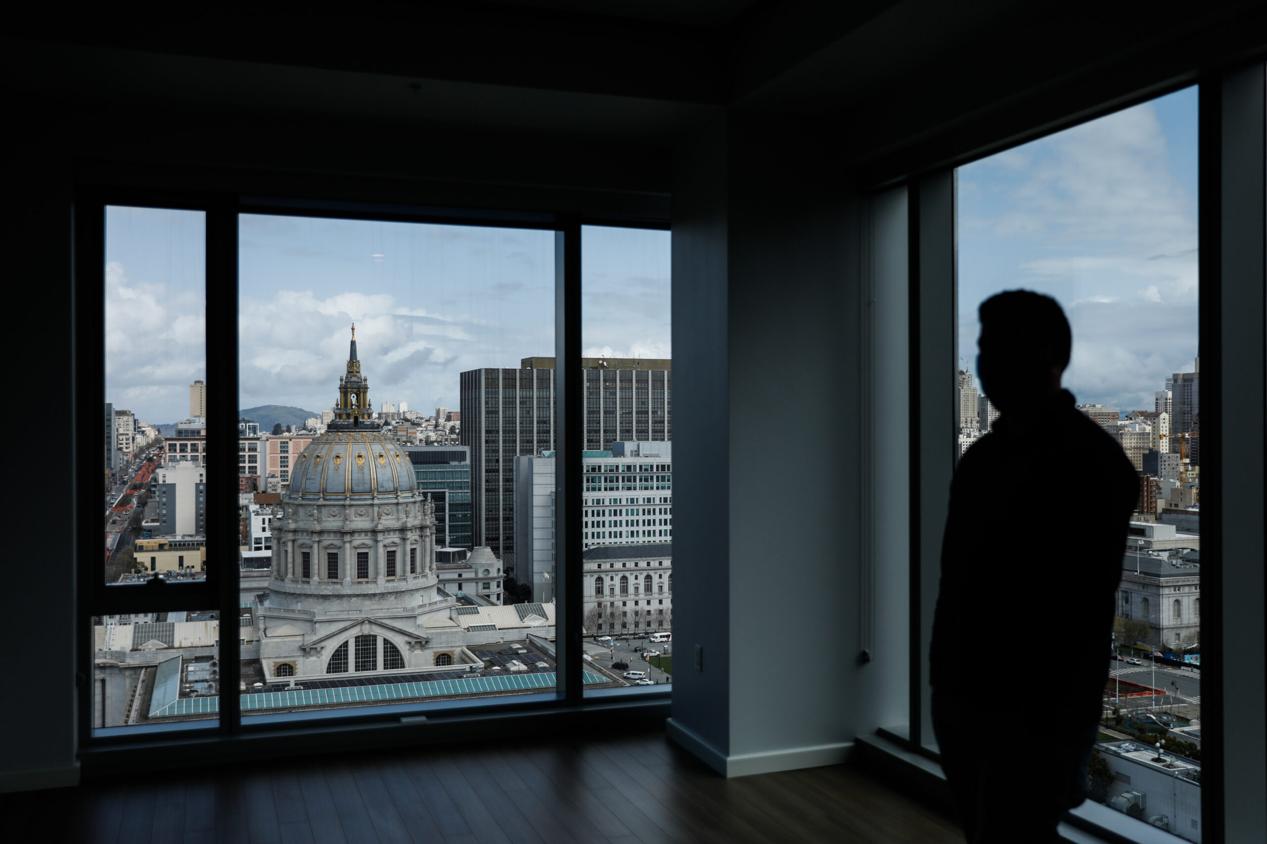 A silhouette of a person stands in a room with a large window, overlooking a cityscape with a domed building.