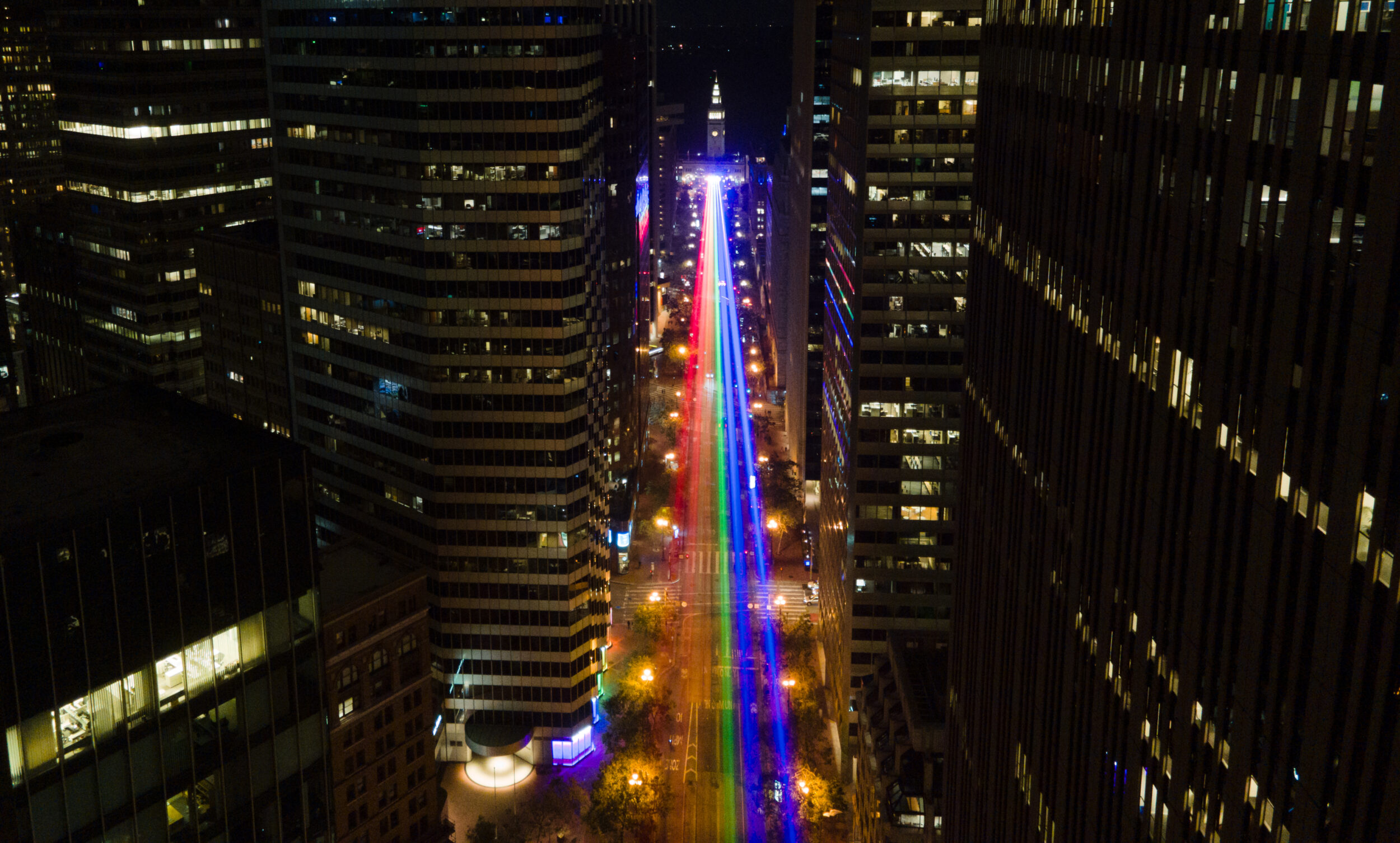A drone view of a rainbow light show down Market Street at night.