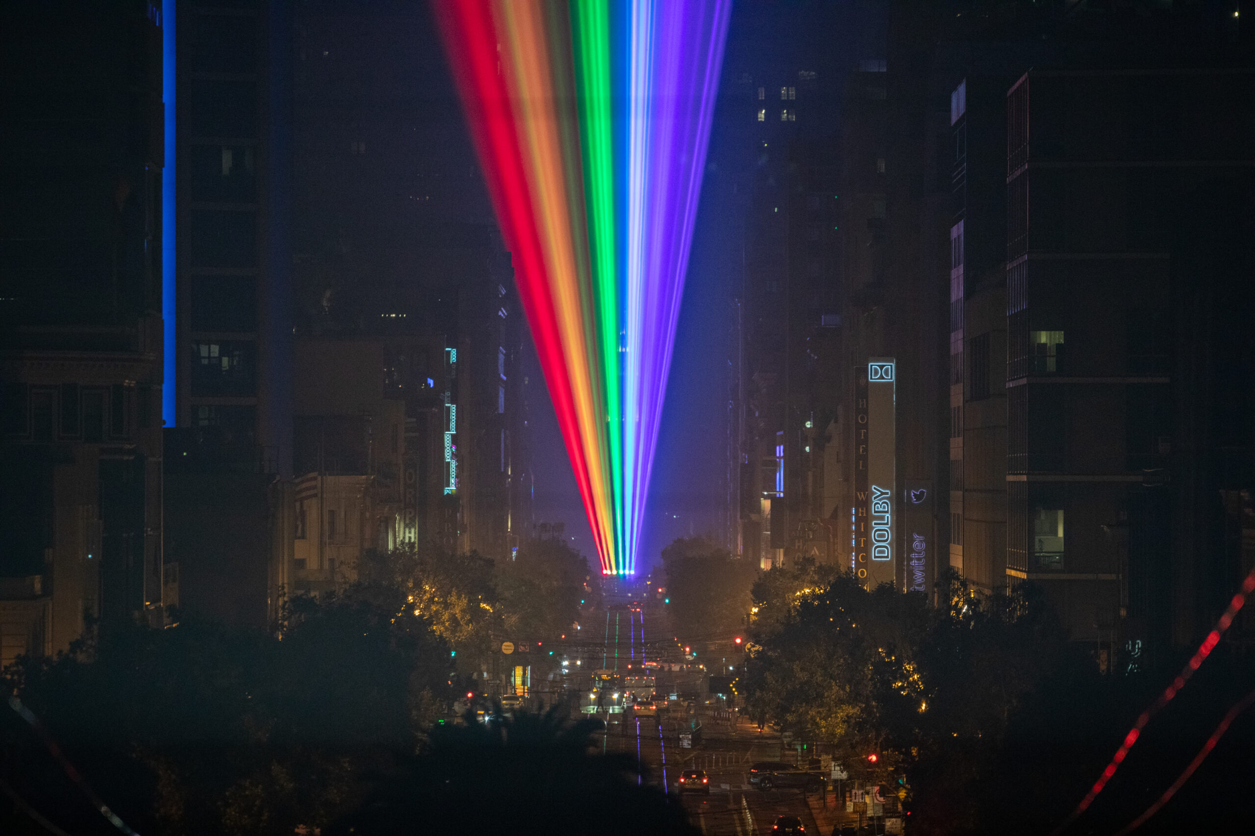 A rainbow of laser lights shines down San Francisco's Market Street at night.