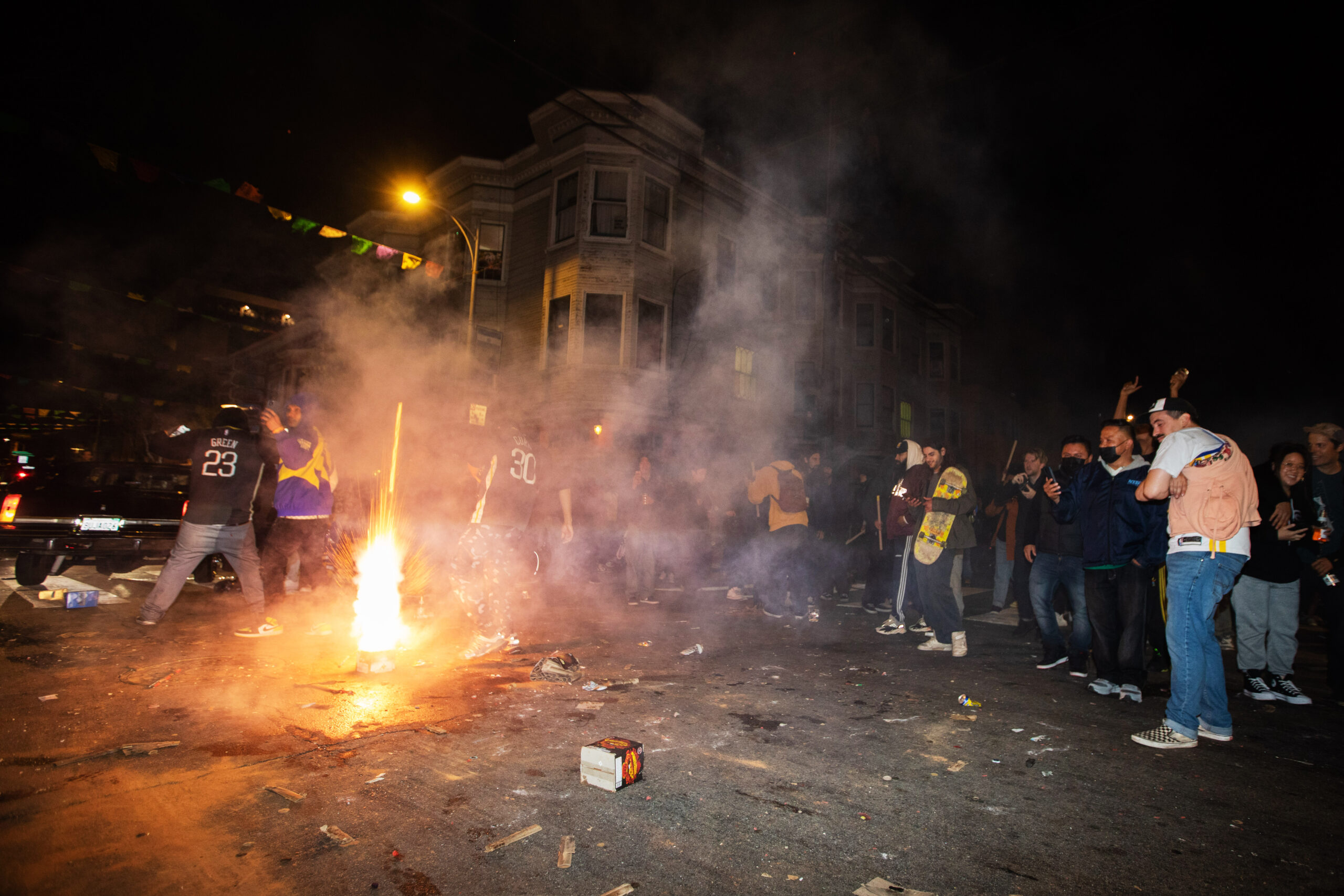 People light illegal fireworks at nighttime in a city street.