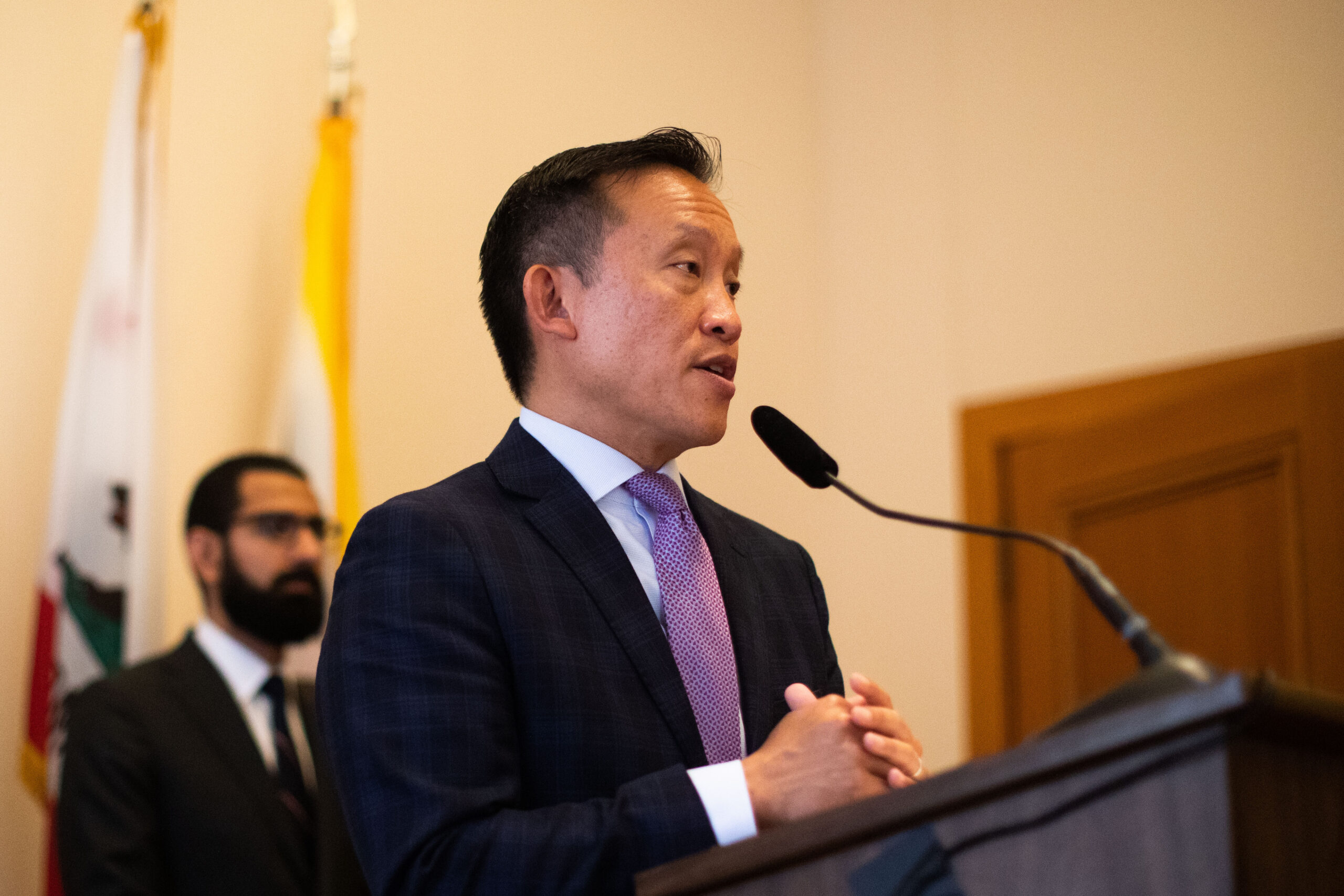 City Attorney David Chin speaks behind a podium in a conference room at San Francisco City Hall. 