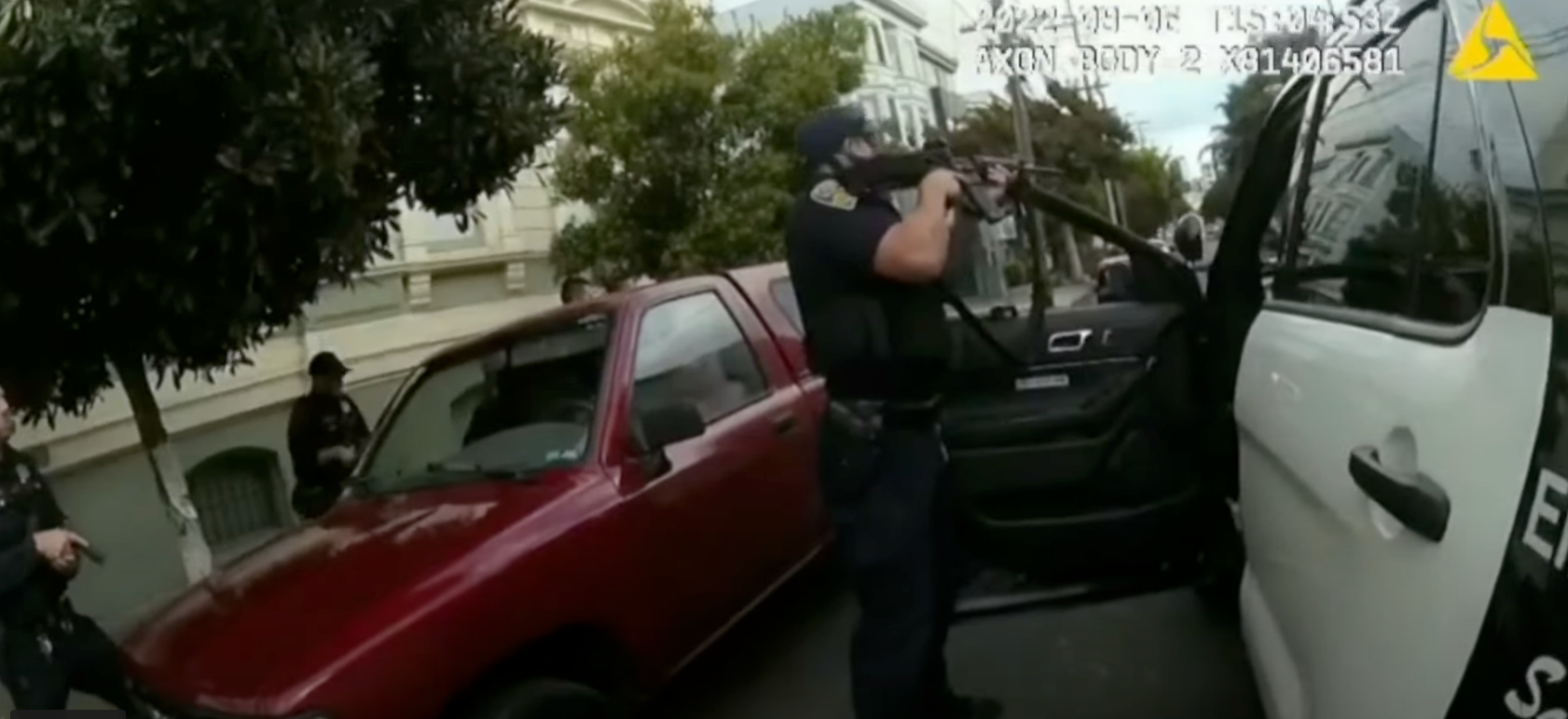 A still from police bodycam footage shows a police officer pointing a rifle.