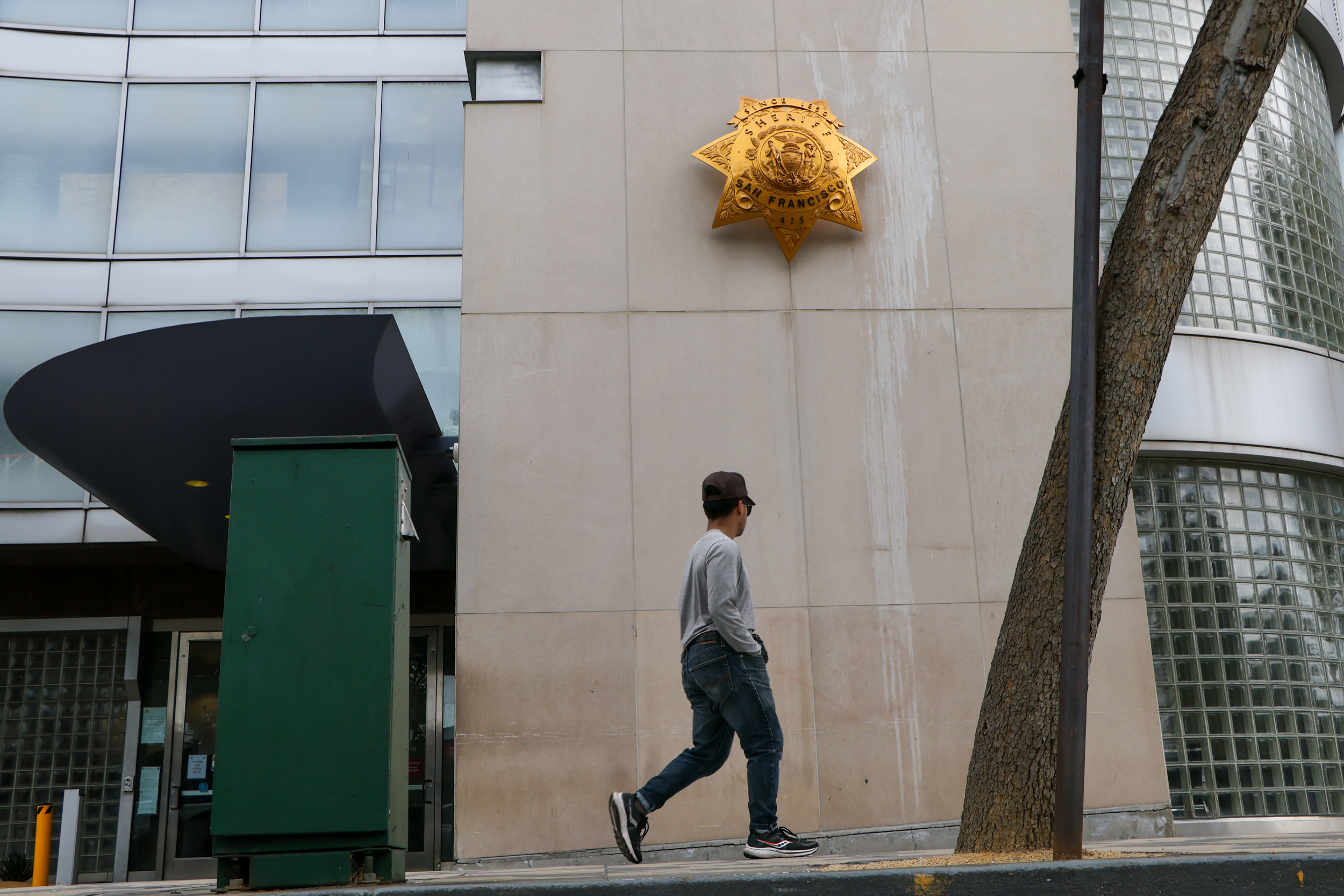 A person walks by a beige colored building with a law enforcement star affixed on the facade