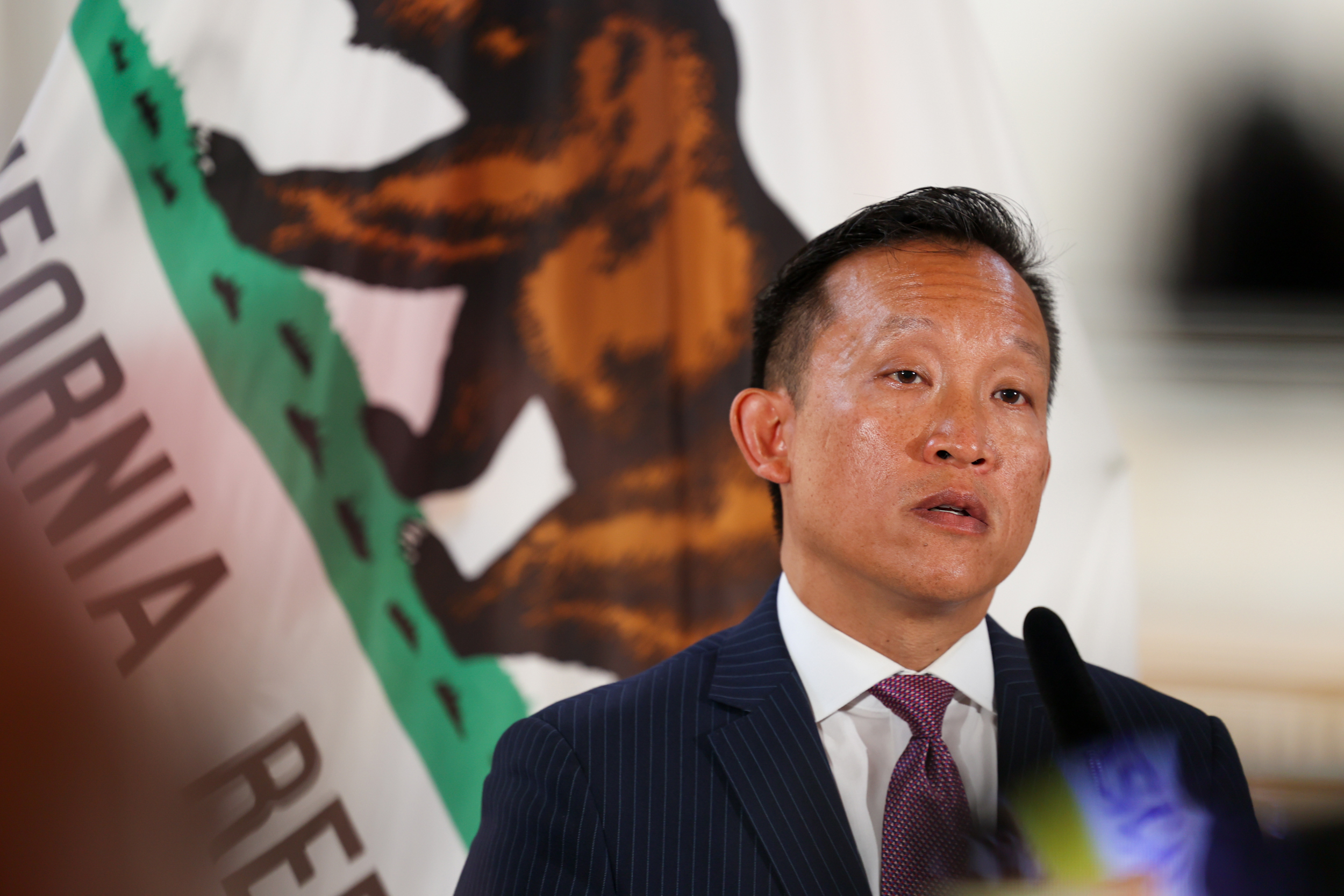 City Attorney David Chiu speaking in front of a California flag.