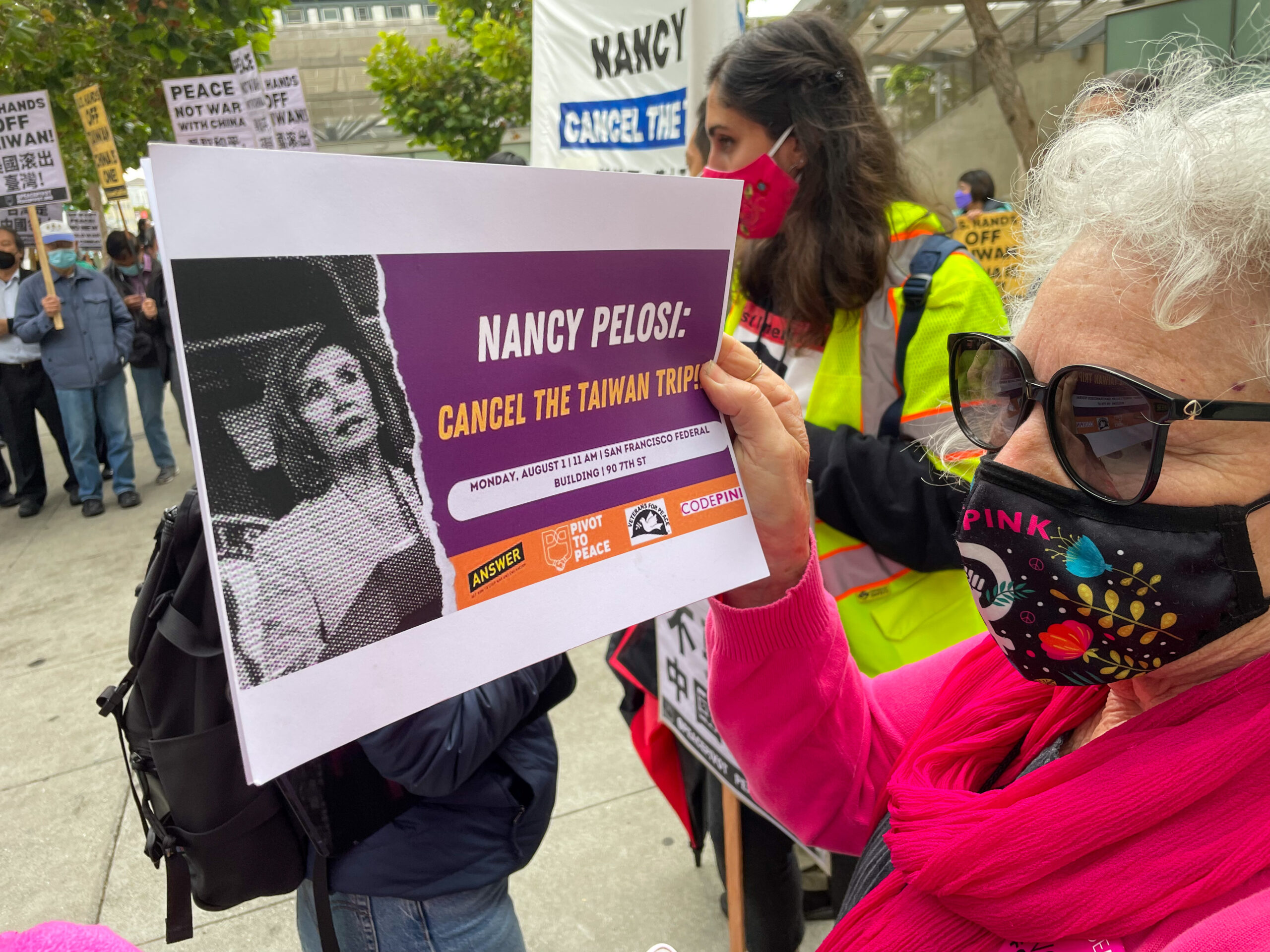 A woman in sunglasses and a mask holds a sign demanding that Nancy Pelosi cancel a planned trip to Taiwan.