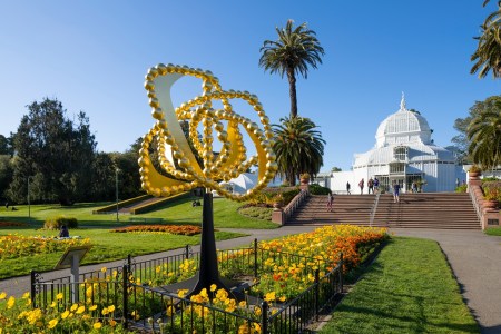 Golden spiral sculpture, colorful flowers, and a white domed conservatory under a clear blue sky.