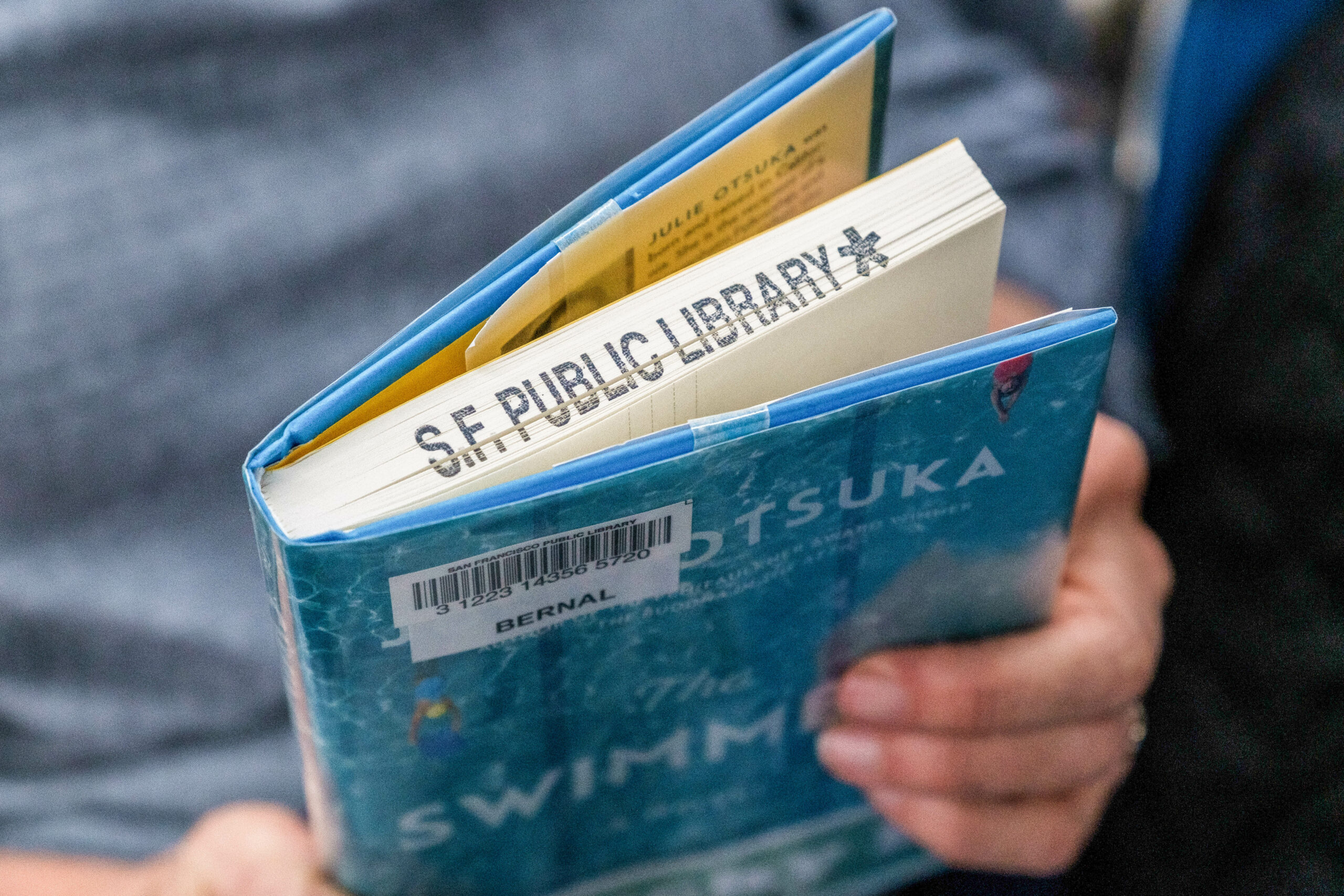 A person holds a book with "S.F. Public Library" stamped on it.
