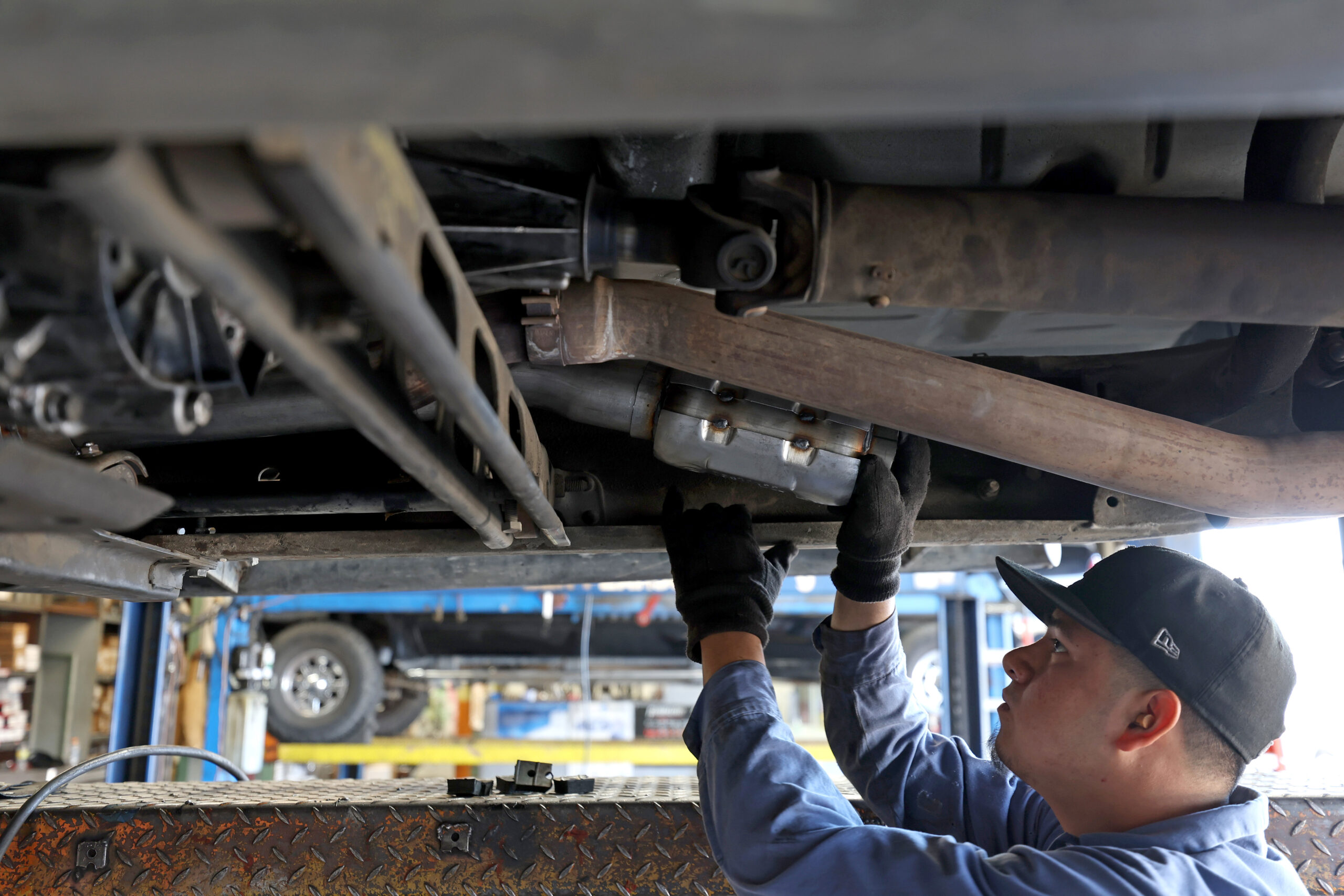 A mechanic works under a lifted vehicle, fixing or inspecting a component.