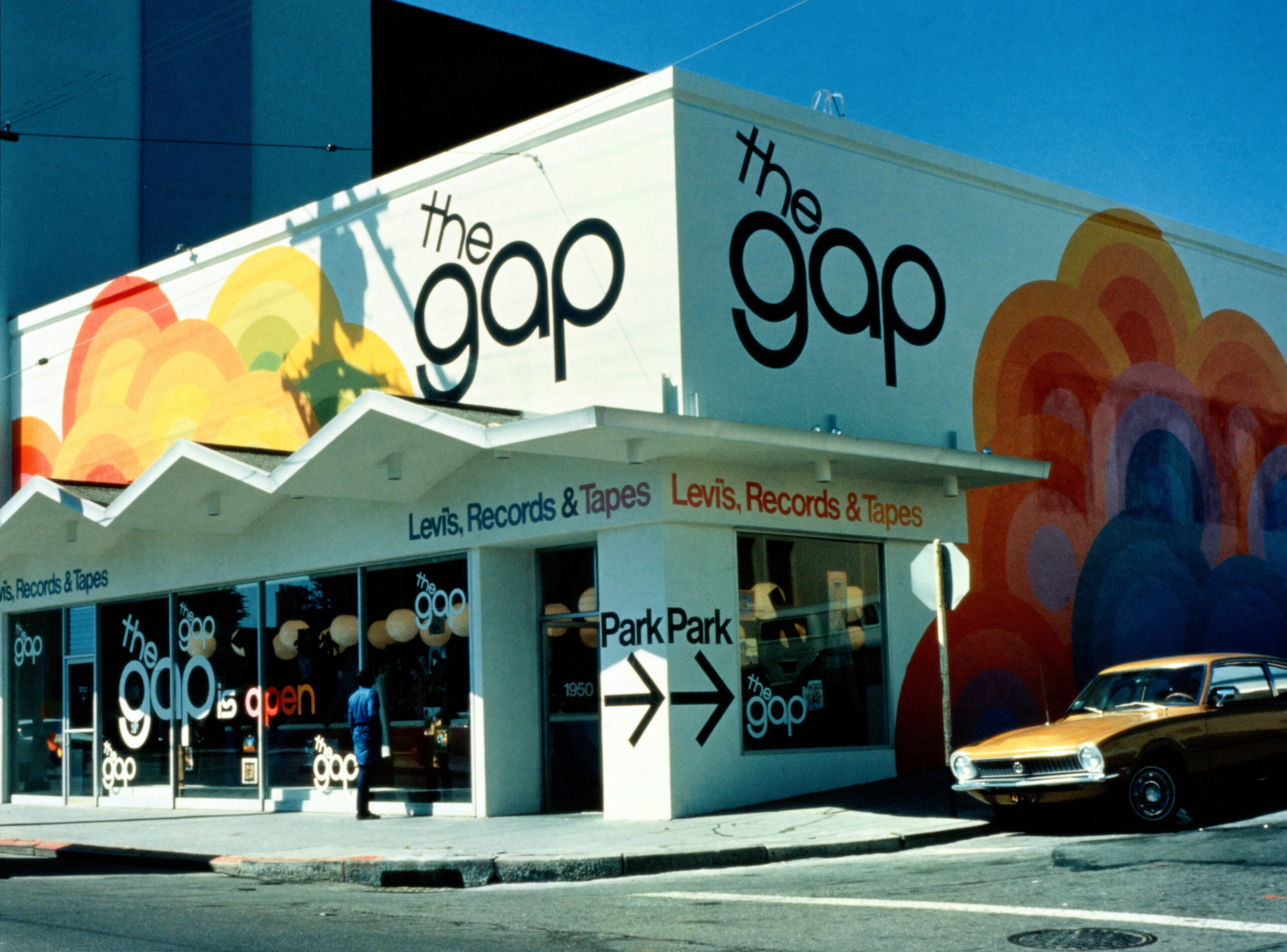 A vintage GAP store with colorful mural, parked retro car, and "Levis, Records & Tapes" signage.