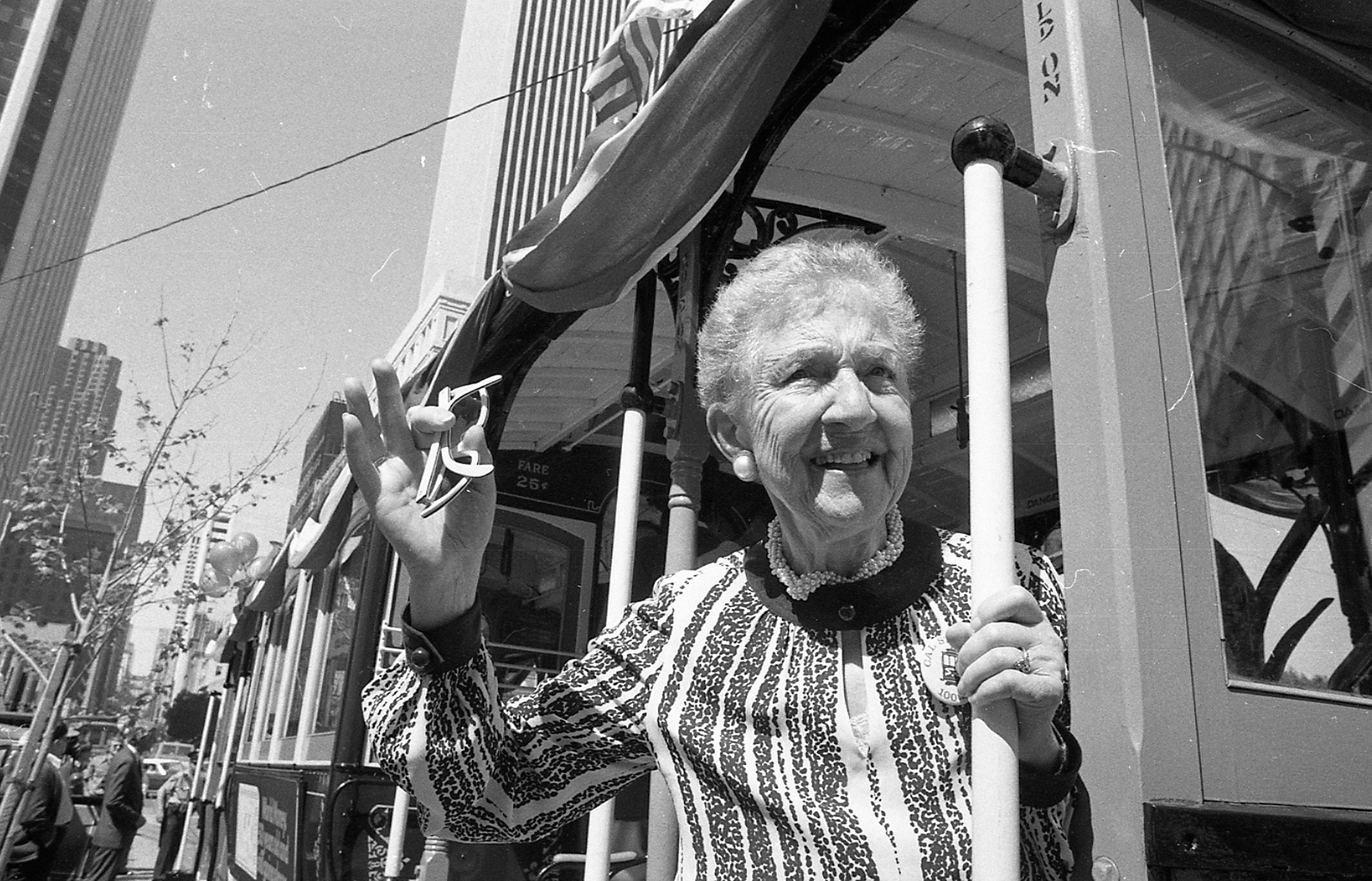An older woman holding keys in her hand holds onto the running board of a San Francisco cable car.
