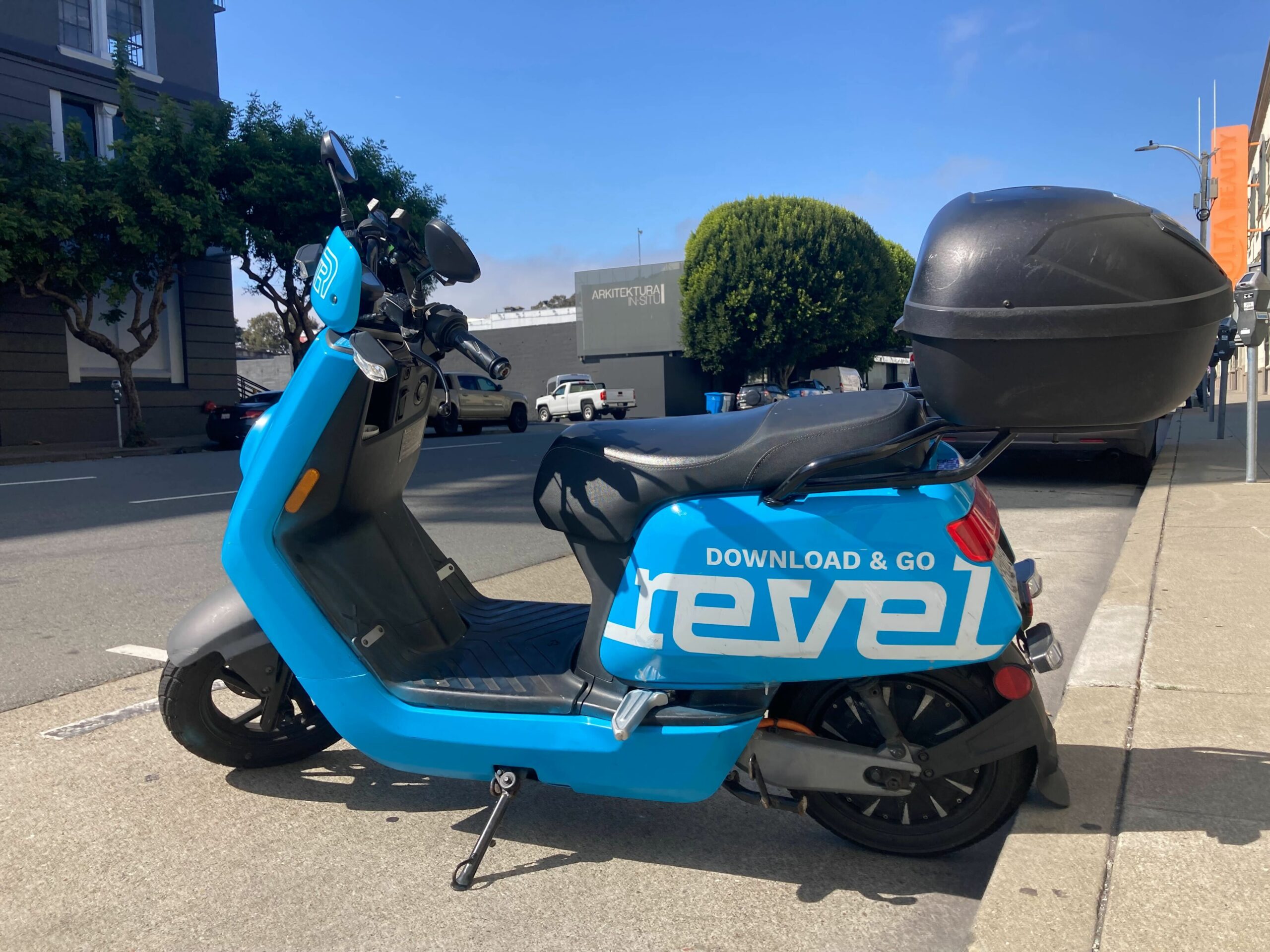 A blue moped is parked with its back wheel against a curb in San Francisco's SoMa neighborhood.