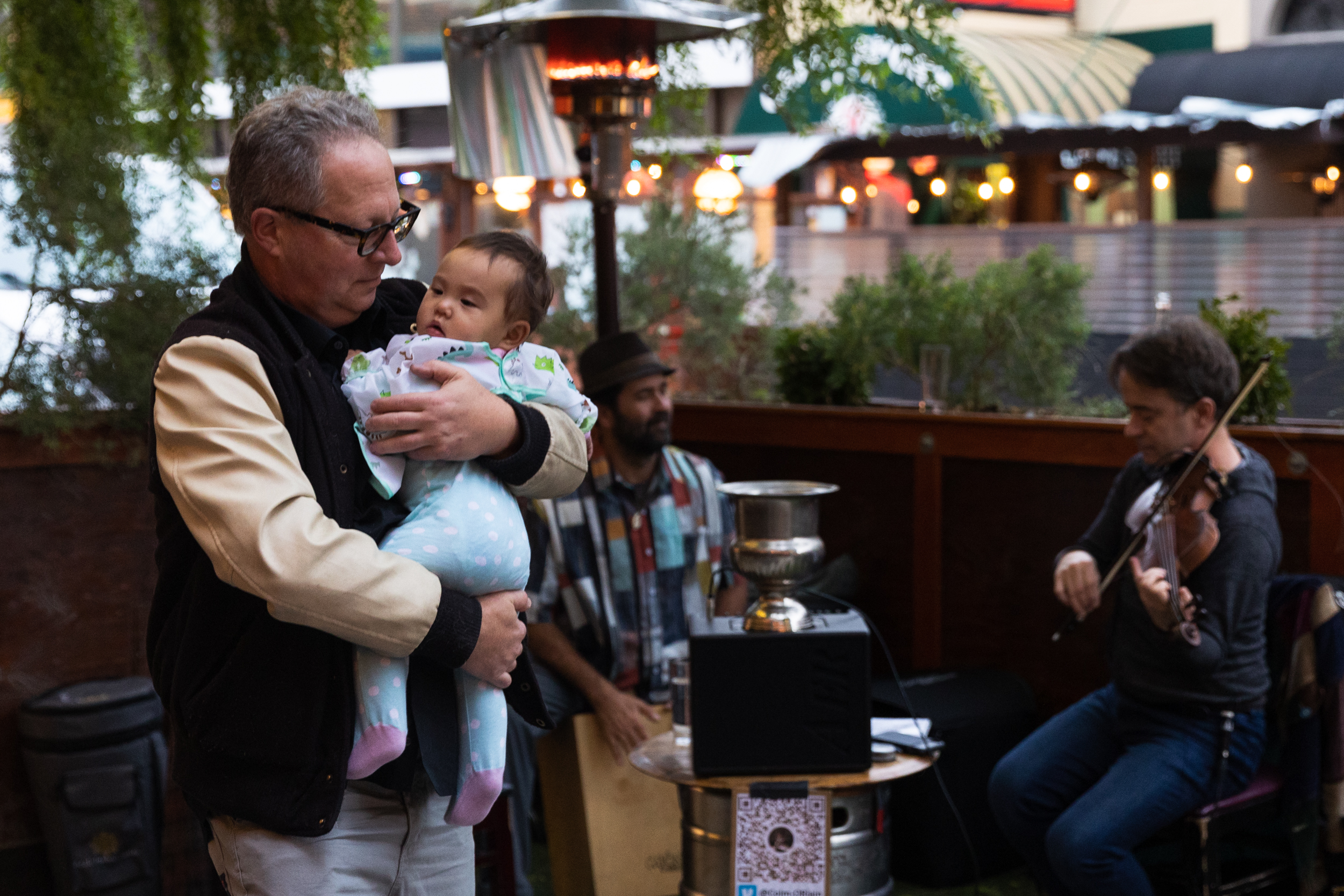 Robert Brownstone dances with Lucy Mae, a friend’s baby, while Colm O’Riain and Wade Peterson perform in the parklet at Belle Cora in the North Beach neighborhood of San Francisco