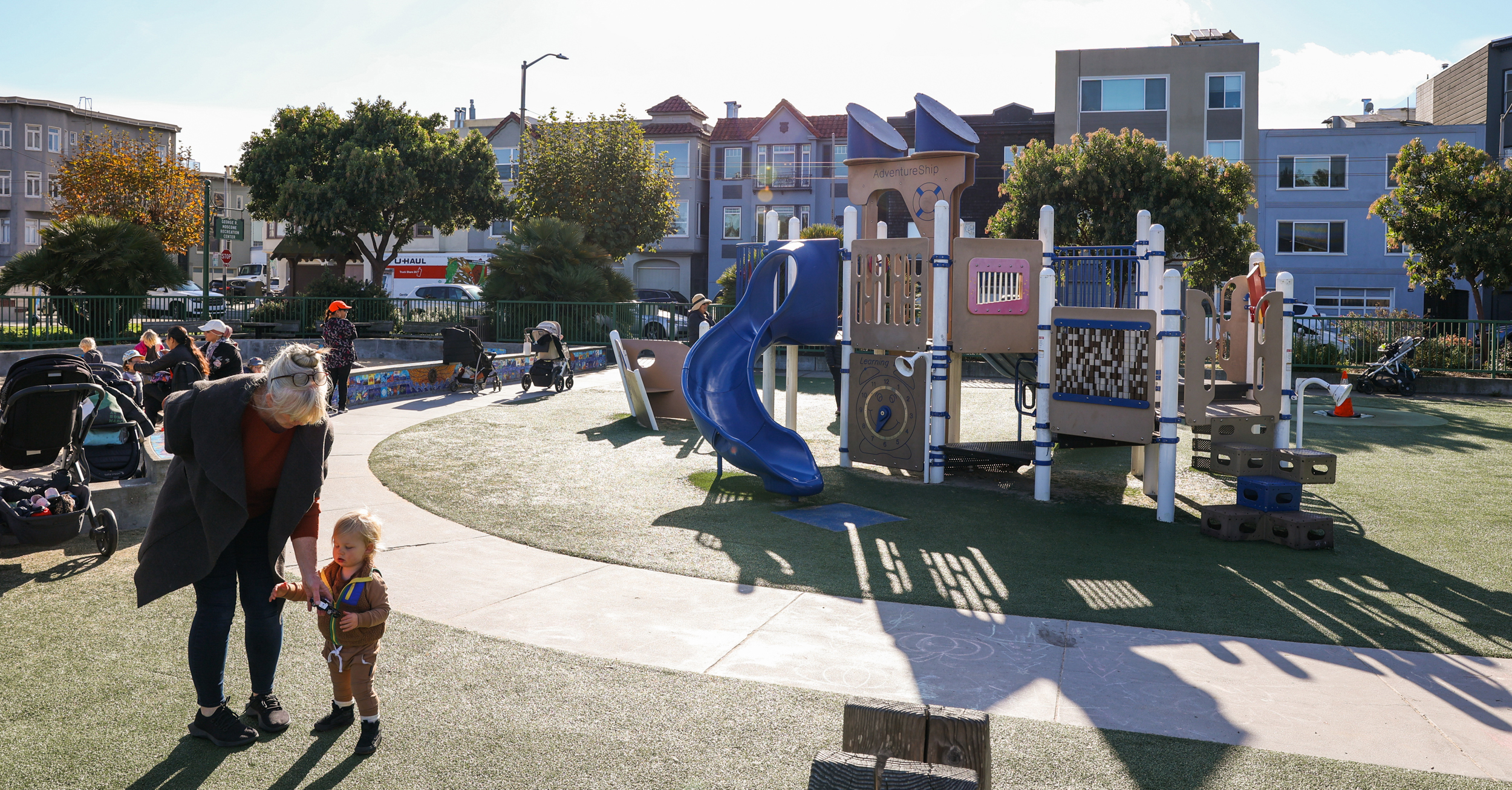 A mother and child stand in front of an outdoor playground in the Marina in San Francisco.