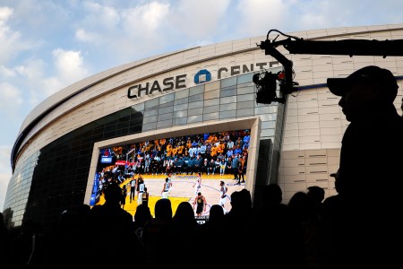 An audience watches a basketball game projected onto a giant screen outside the Chase Center.