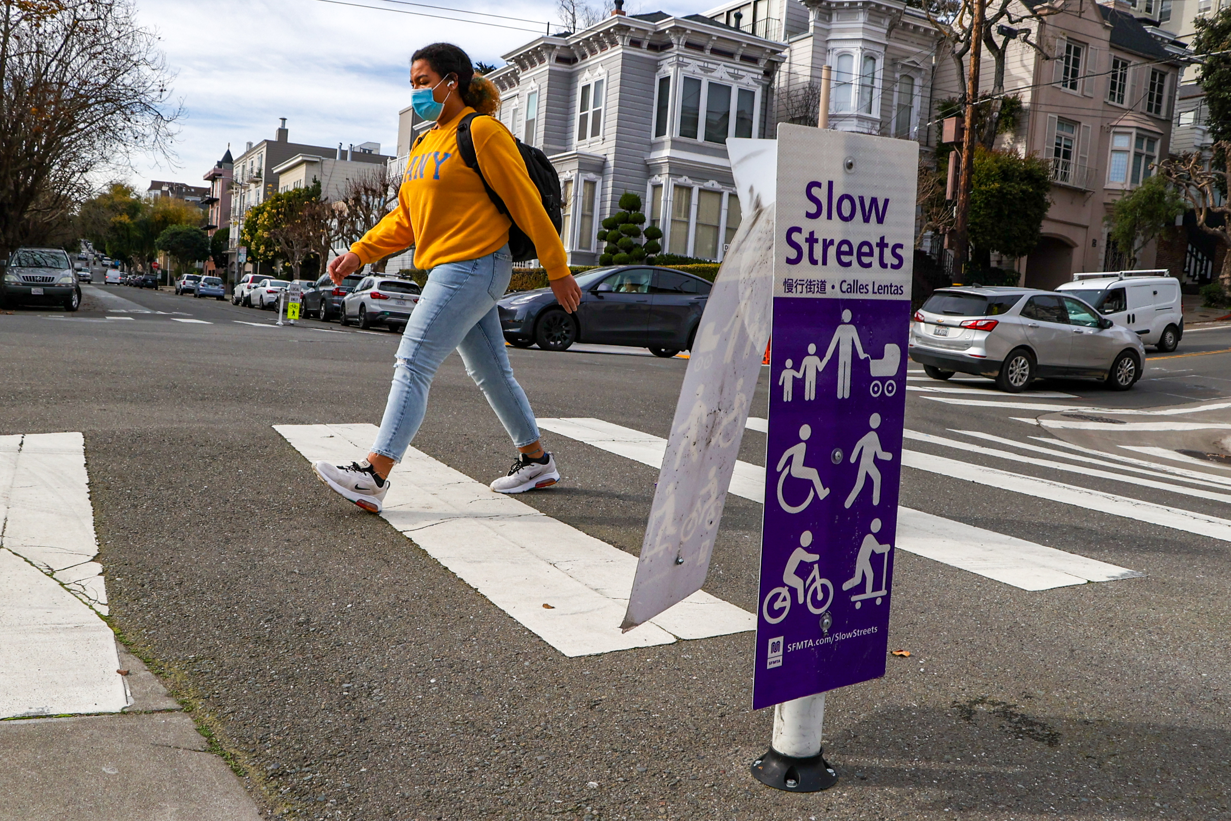 A pedestrian crosses a city street near a &quot;Slow Streets&quot; sign.
