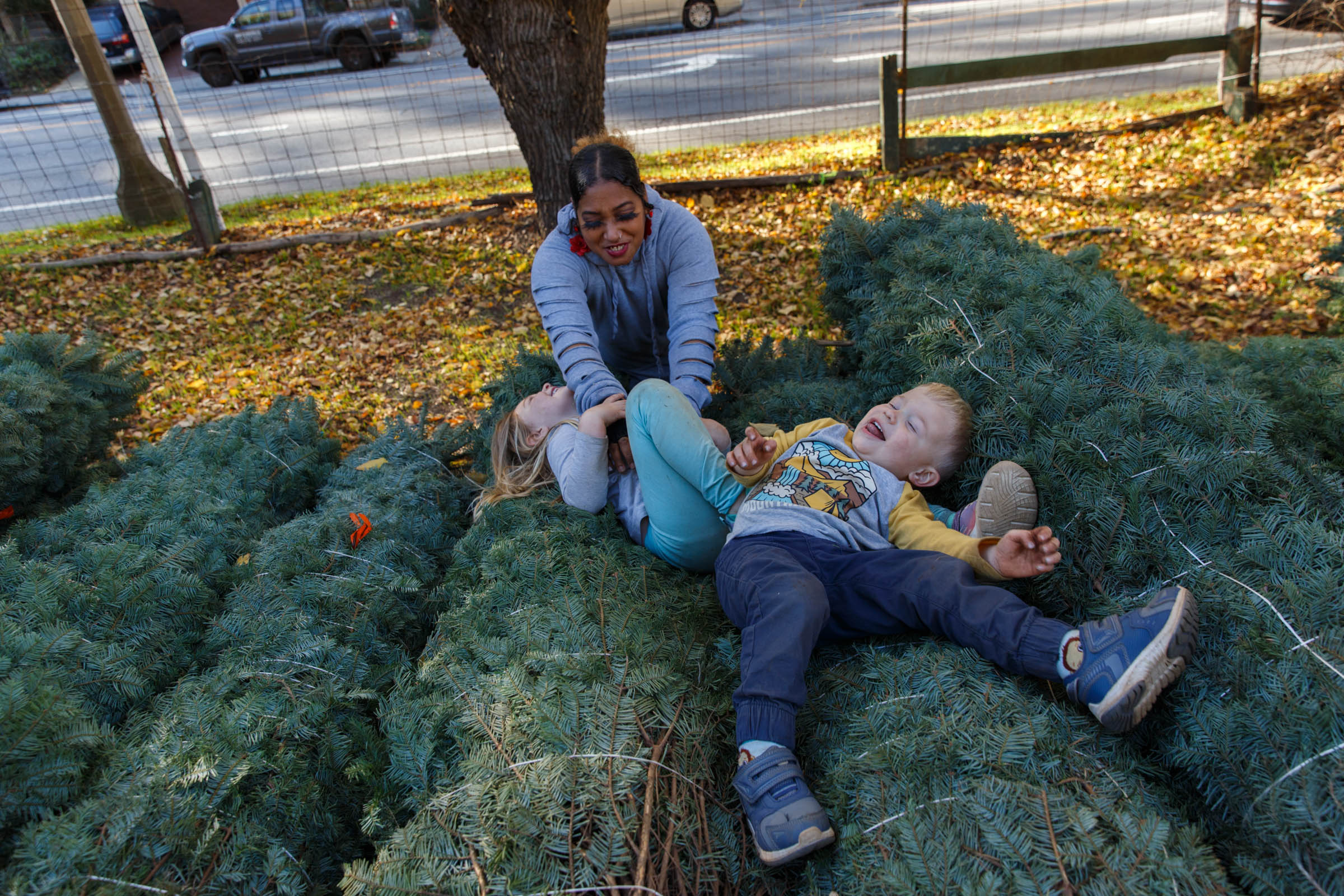 A woman and child play on a pile of wrapped up Christmas trees.