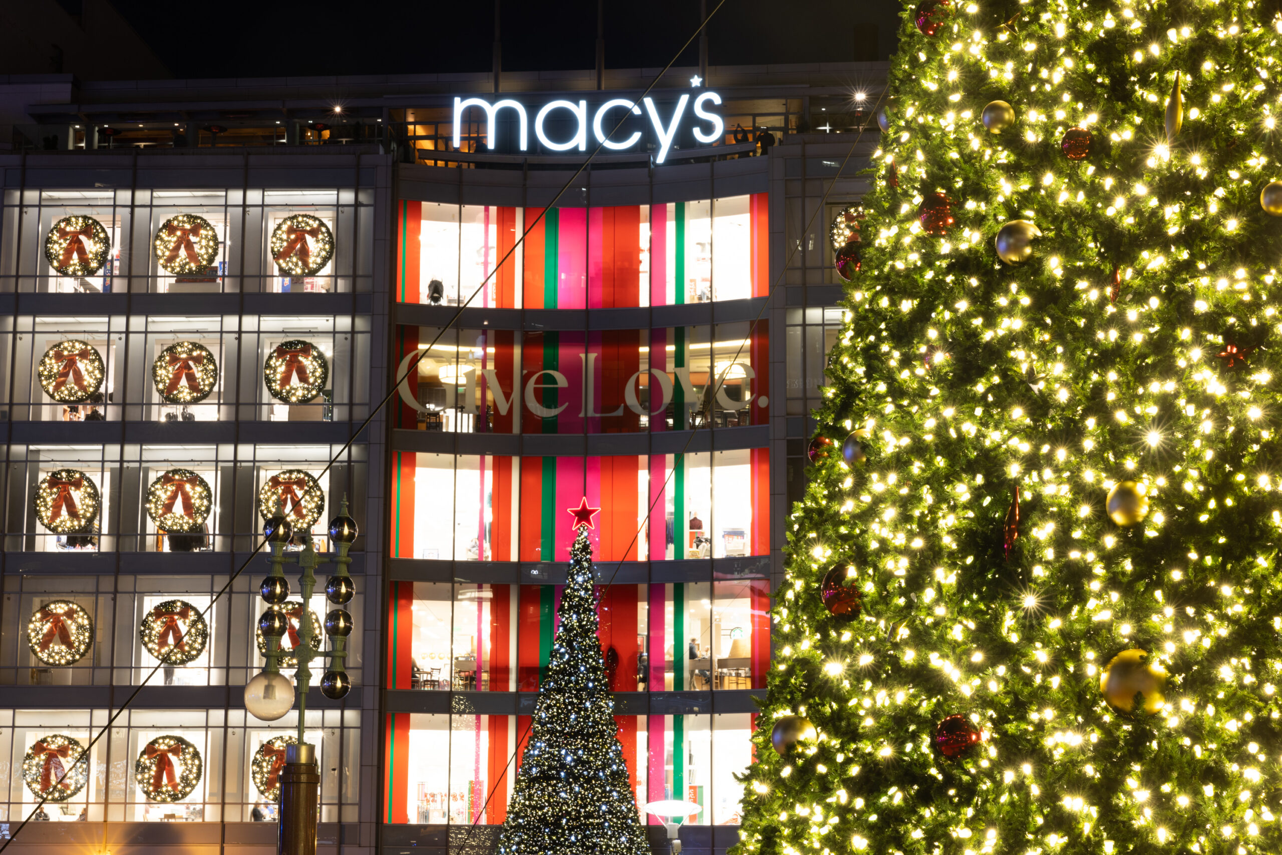 A Christmas tree is lit up in front of the illuminated storefront of Macy's in San Francisco's Union Square. 