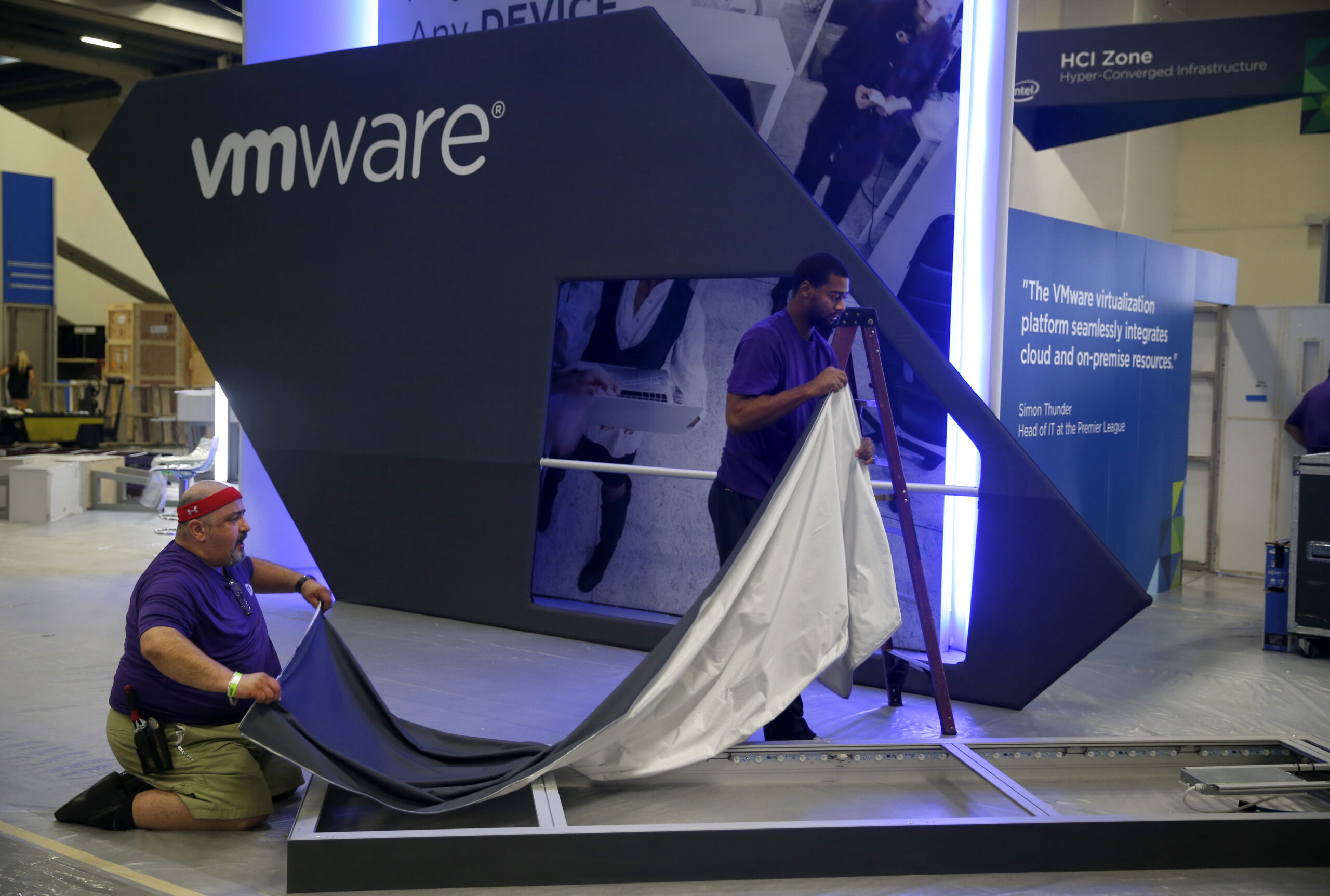 Two men set up a large VMware booth displaying tech branding and quotes at an event venue.