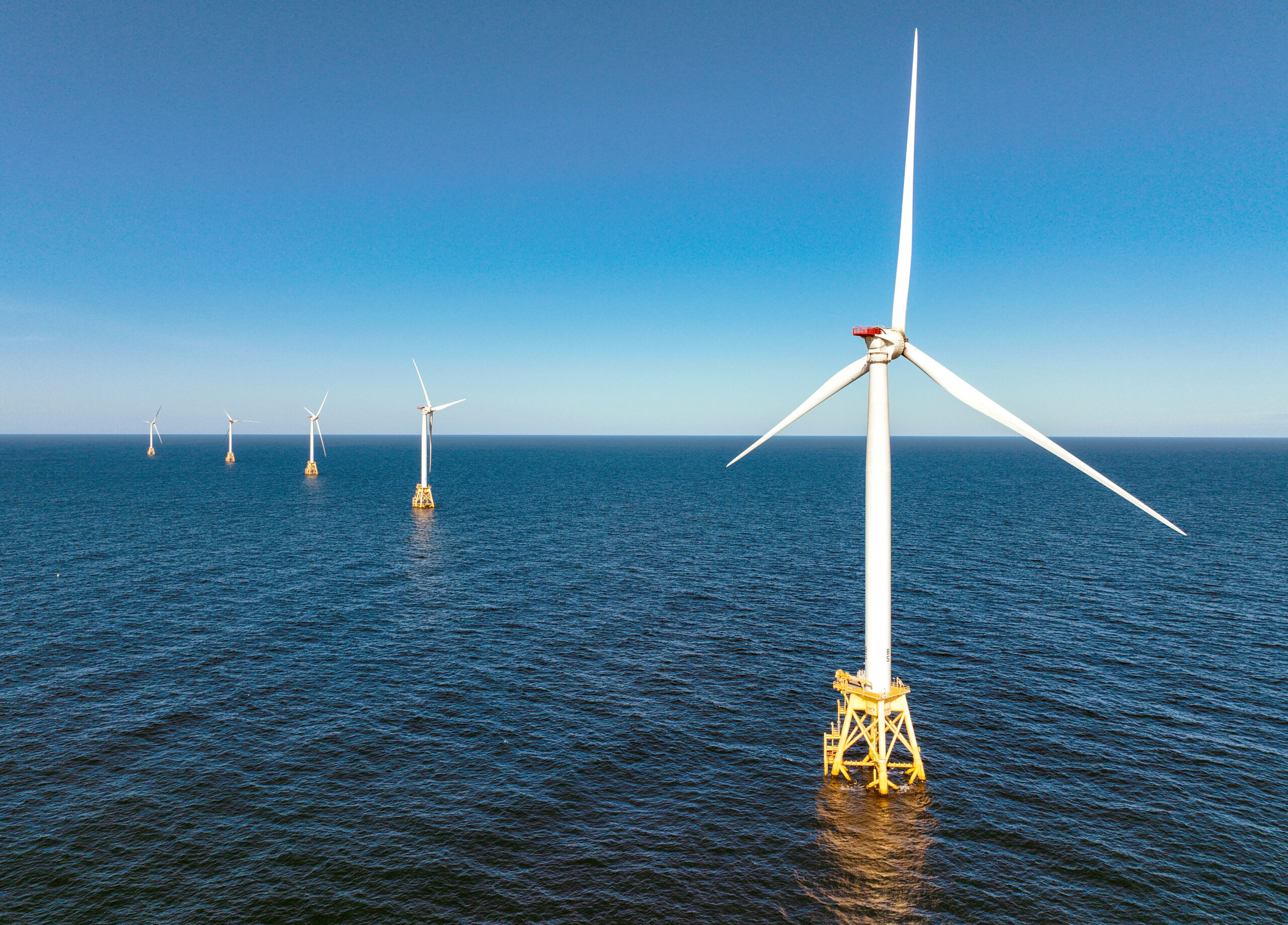 Offshore wind turbines stand in a calm blue sea under a clear sky.