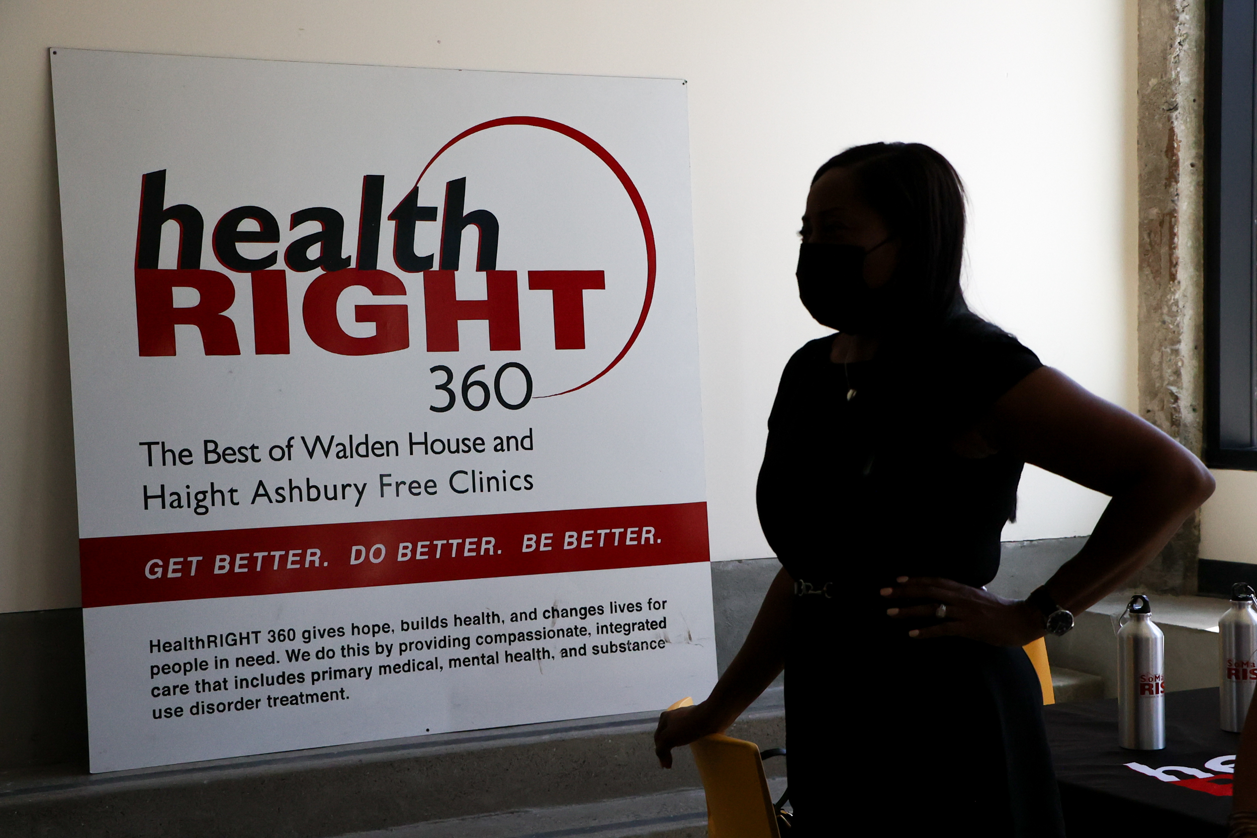 A silhouette of a masked person stands beside a HealthRIGHT 360 sign with motivational slogans.