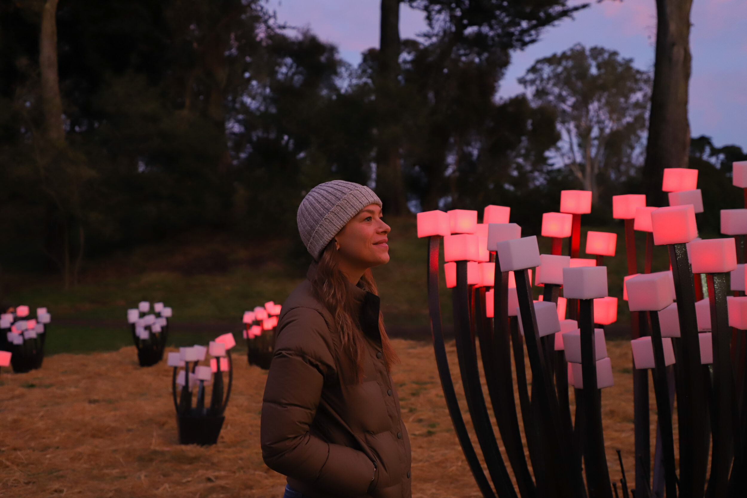 A woman in a beanie looks at an art installation of red cubes in the shape of shrubs.