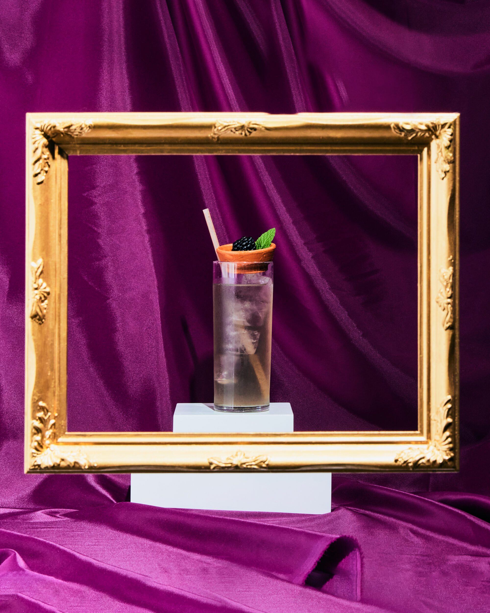 A cocktail is artfully presented in a picture frame as it it were in a museum.