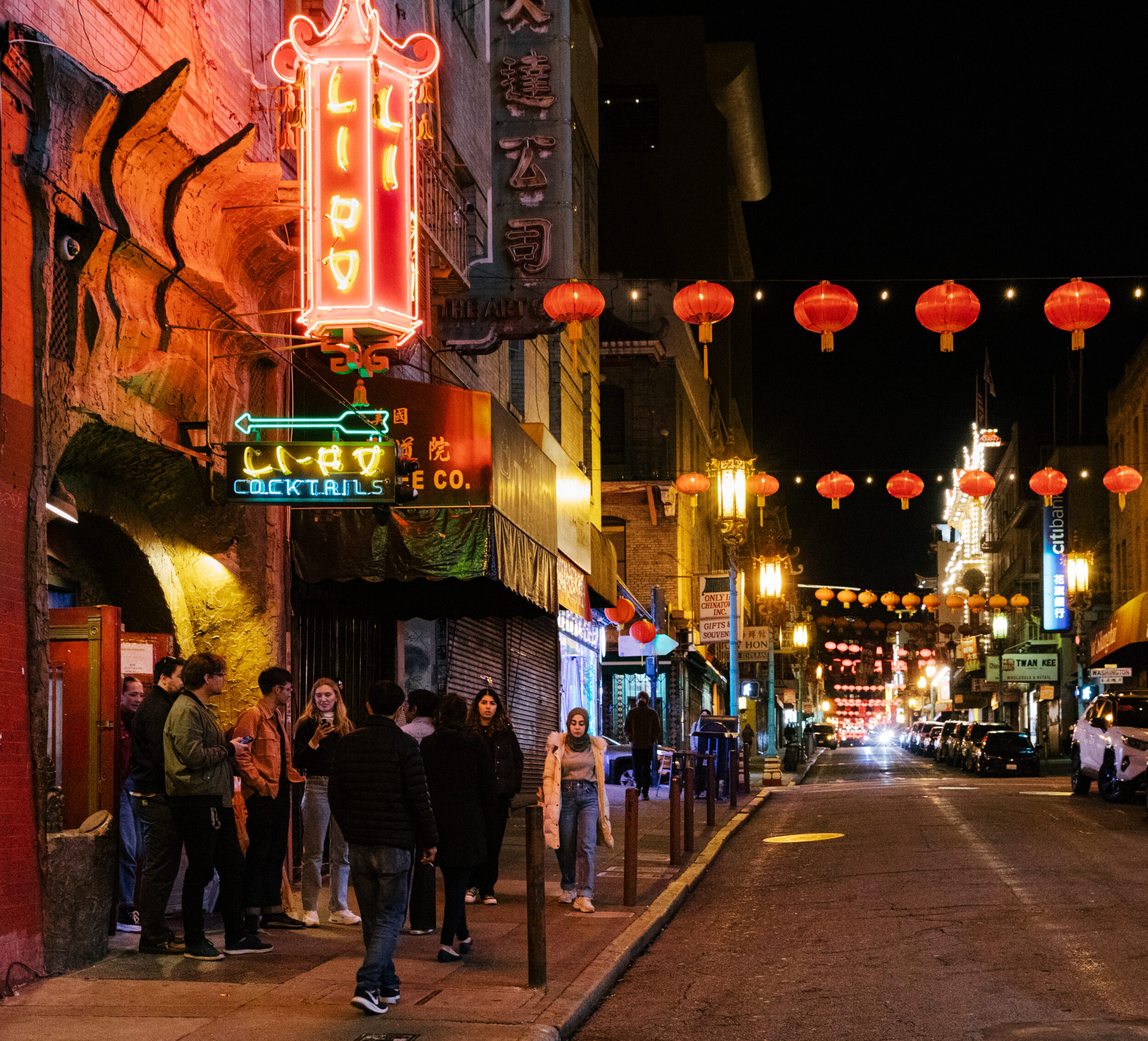 The Li Po loung is lit up with neon on a dark street in San Francisco's Chinatown, where the street is strung with red lanterns.