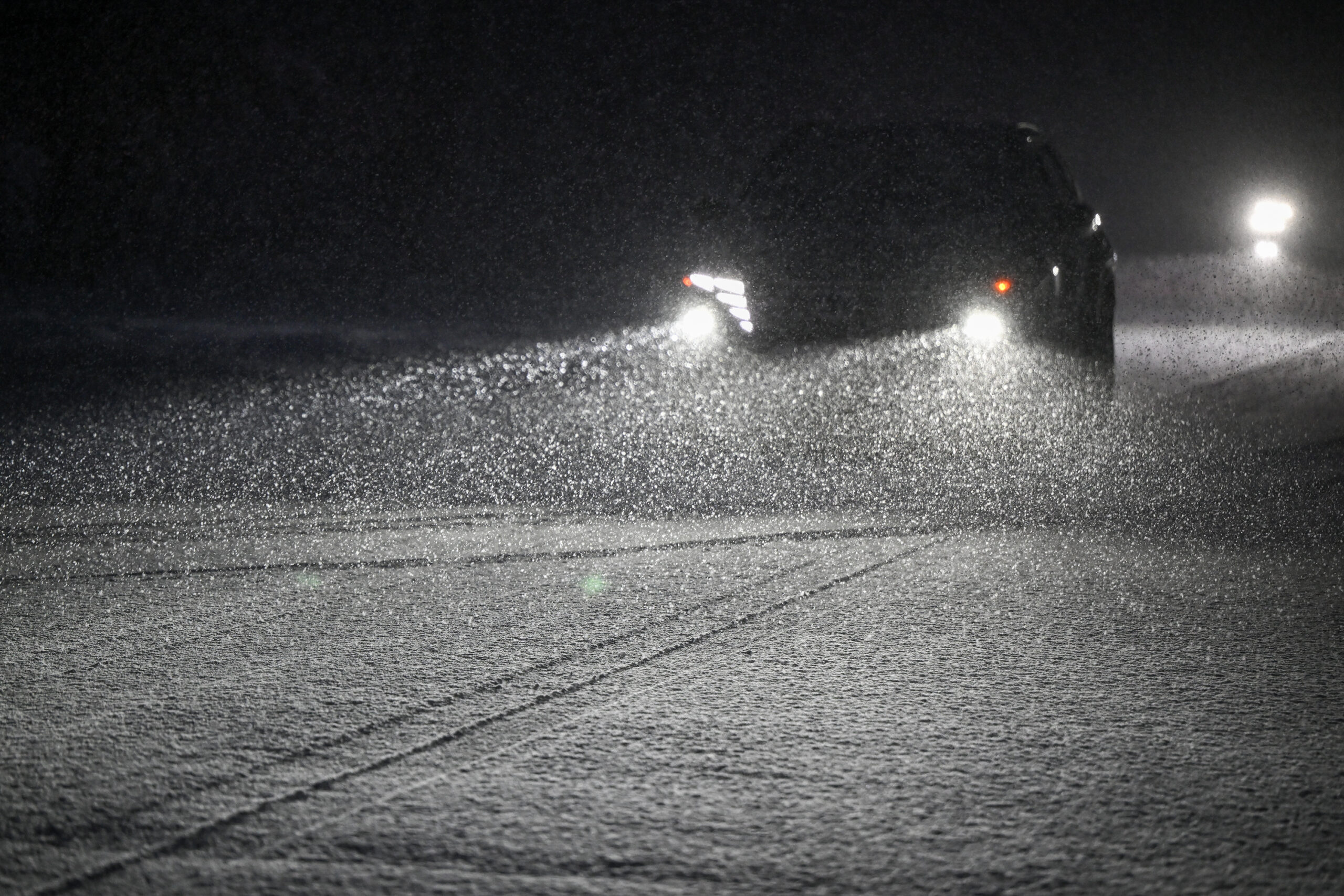 A car driving at night on a snowy road, with headlights reflecting off raindrops.