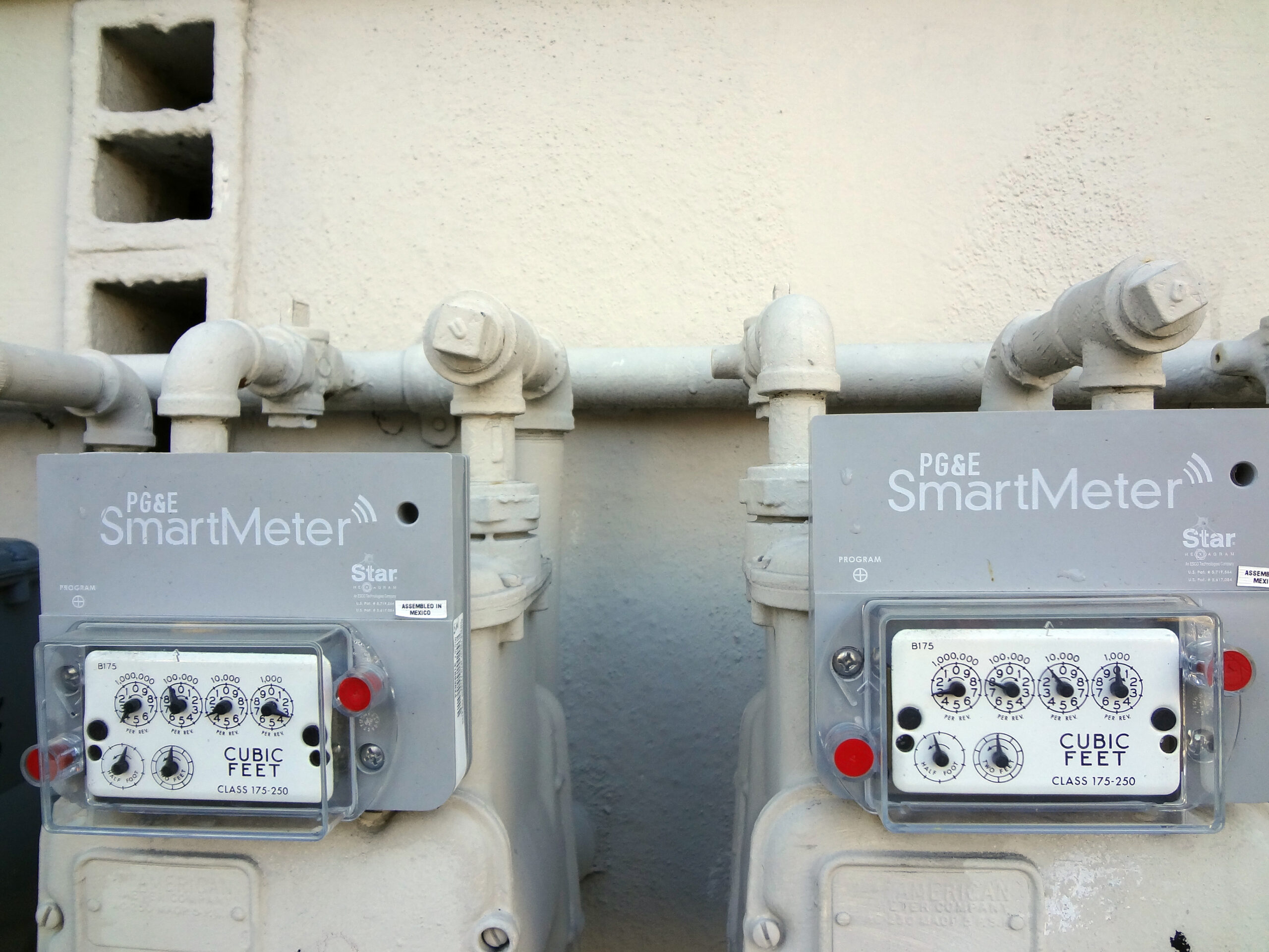 Two PG&E SmartMeters are attached to a wall with pipes above and below them.
