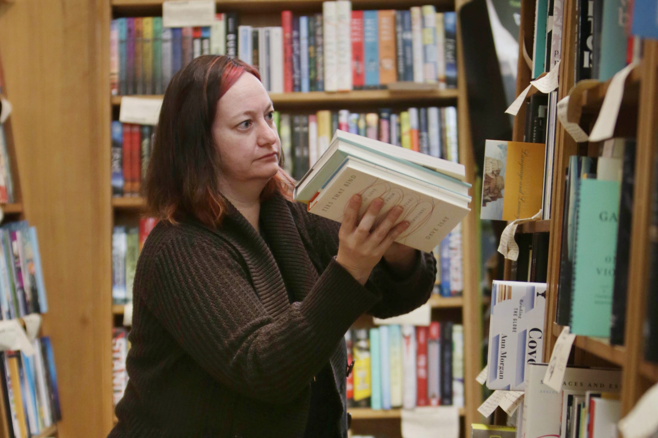A person in a bookstore is shelving books, with a focused expression. Shelves full of colorful books line the background, creating a cozy, literary atmosphere.