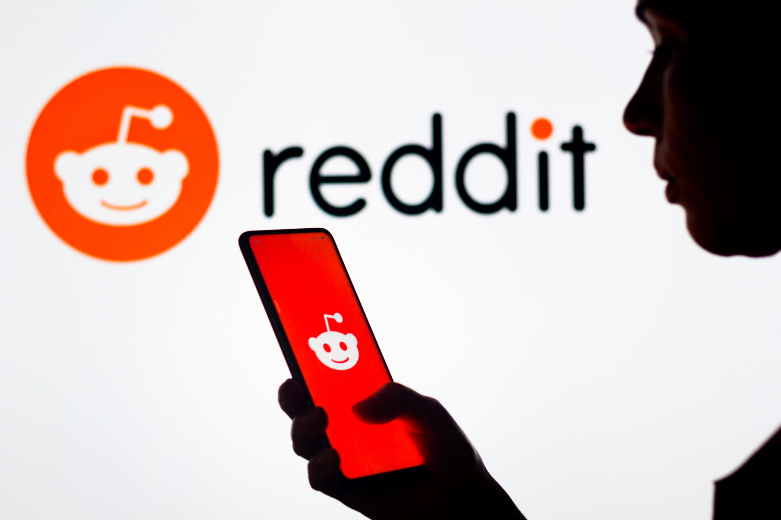 In this photo illustration, a woman’s silhouette holds a smartphone with the Reddit logo displayed.
