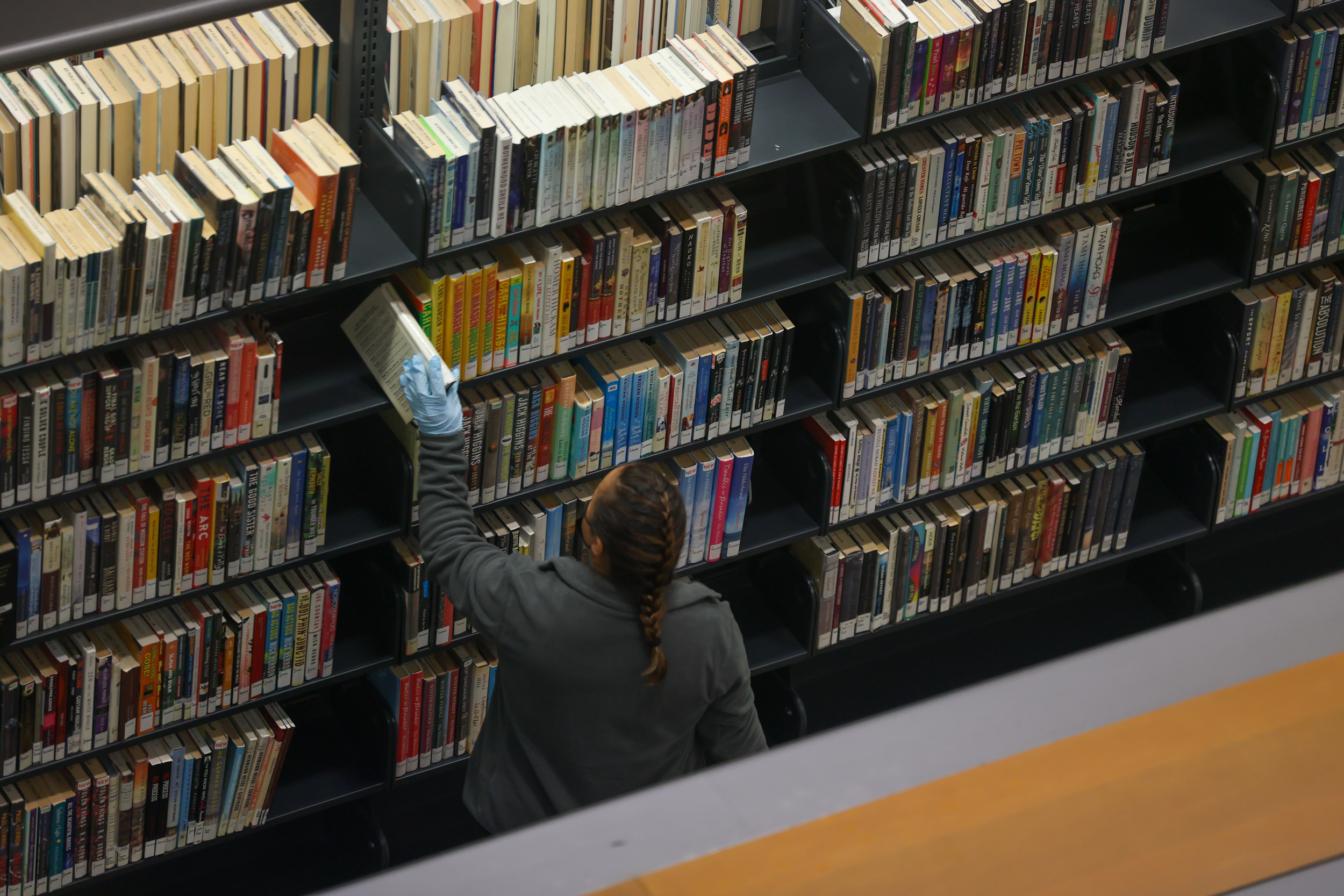 A person is reaching for a book on a high shelf in a library with many books.
