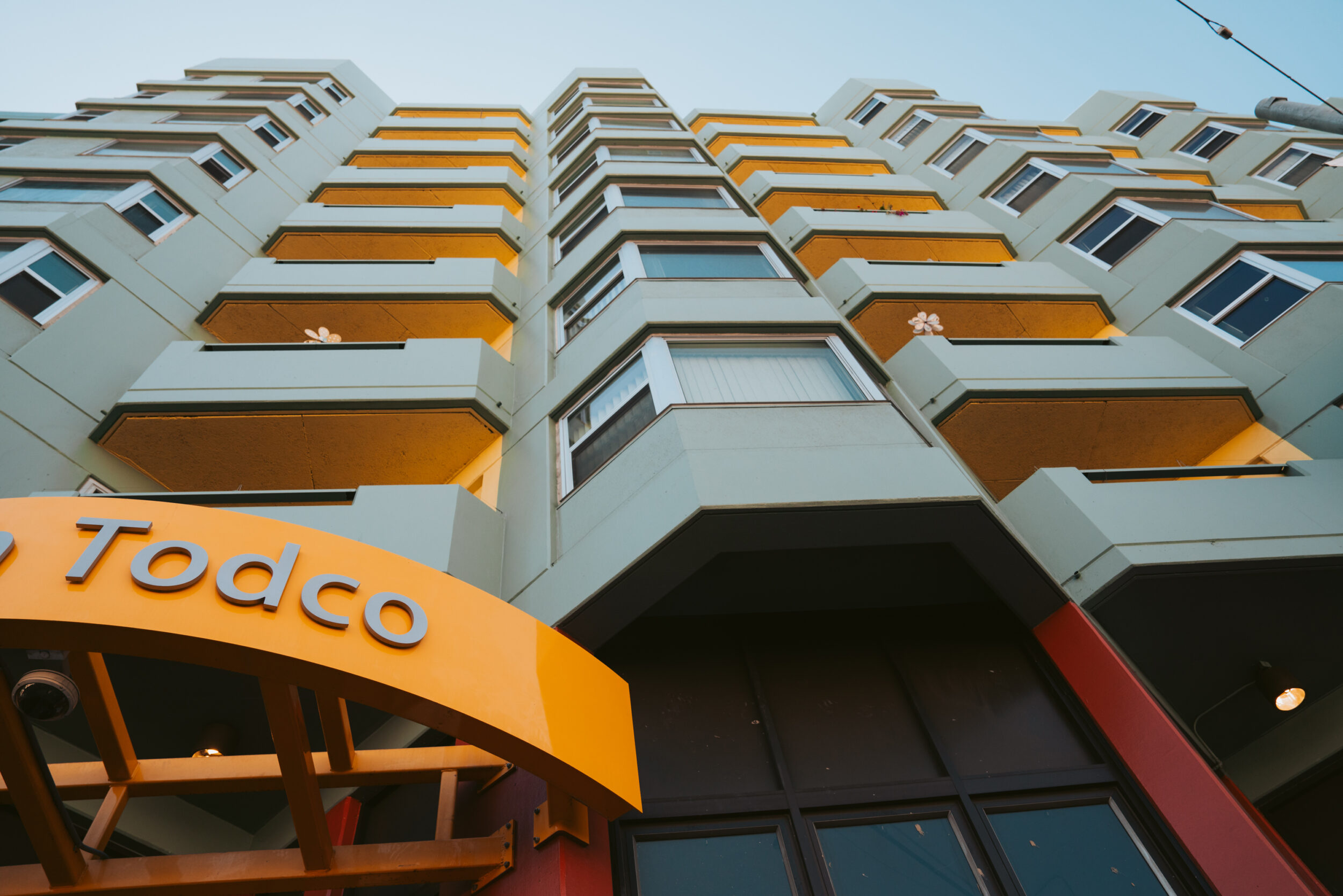 A colorful building facade with staggered balconies, under a clear sky, marked &quot;Todco&quot; on an orange overhang.