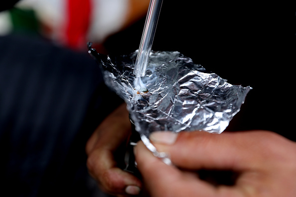 Hands holding foil with a straw inserted, likely a makeshift device, with a blurred background.