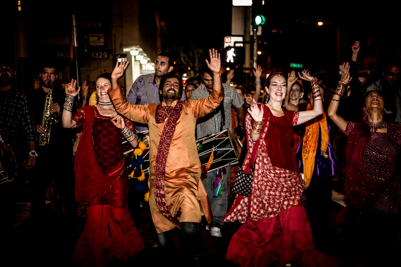 People in traditional Indian attire are dancing joyfully at night on a city street.