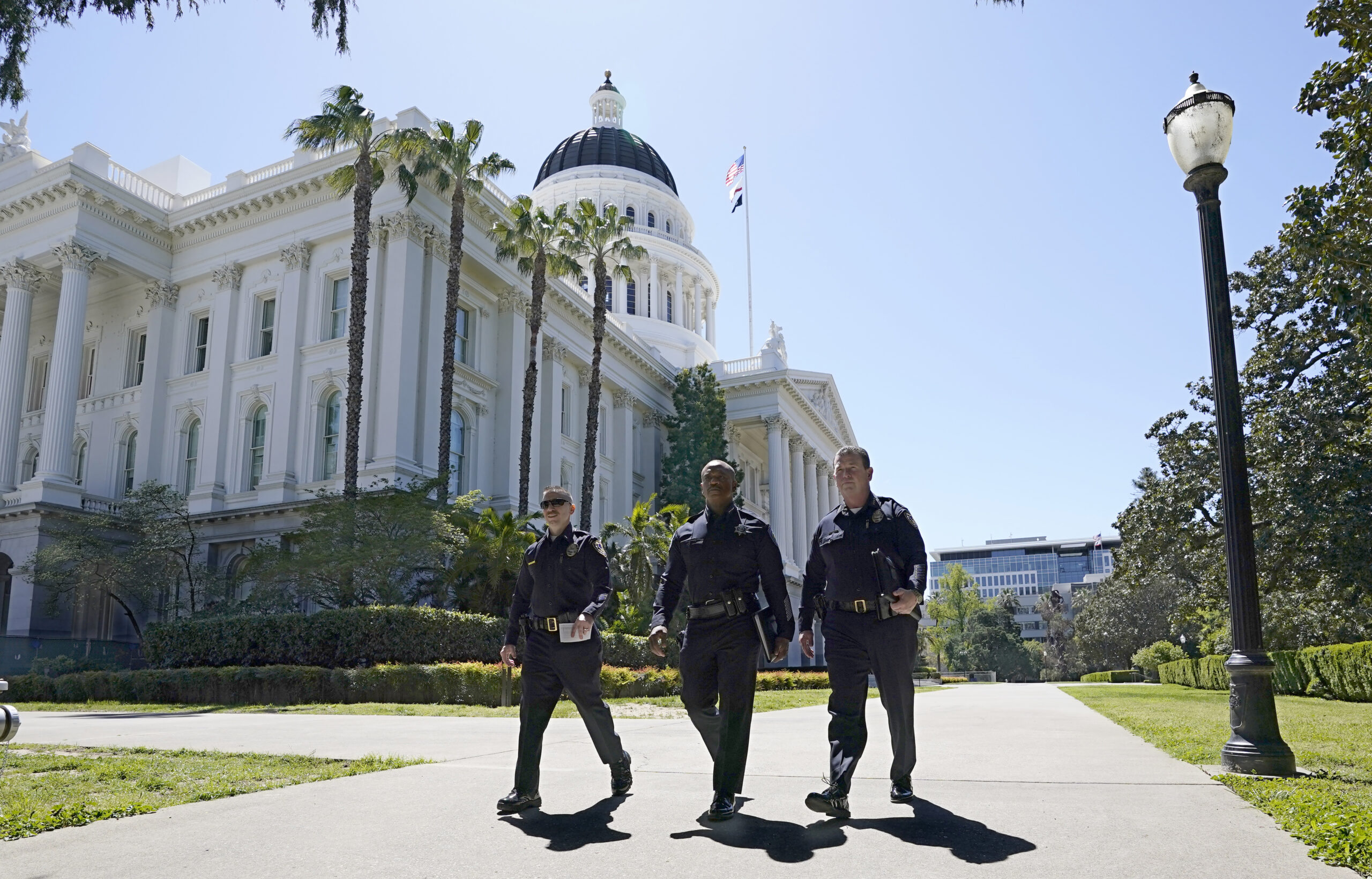 Three people walk past the California Capitol building