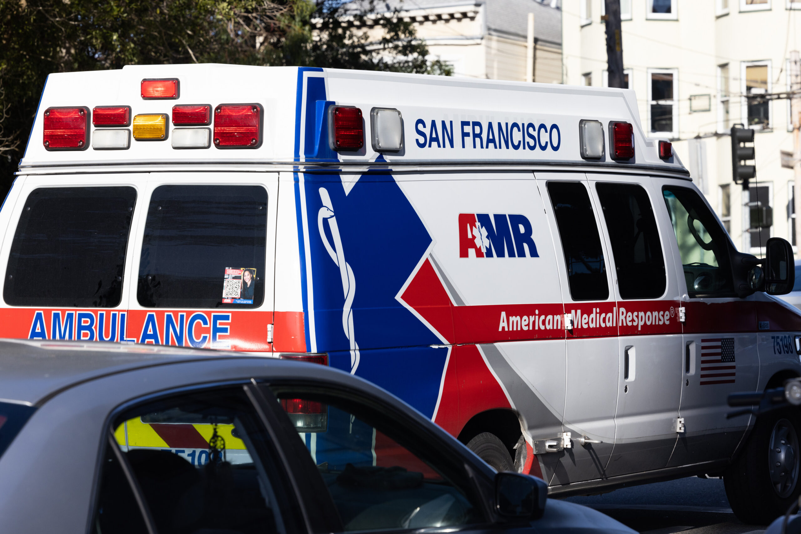 A white ambulance with blue and red markings passes hospital building