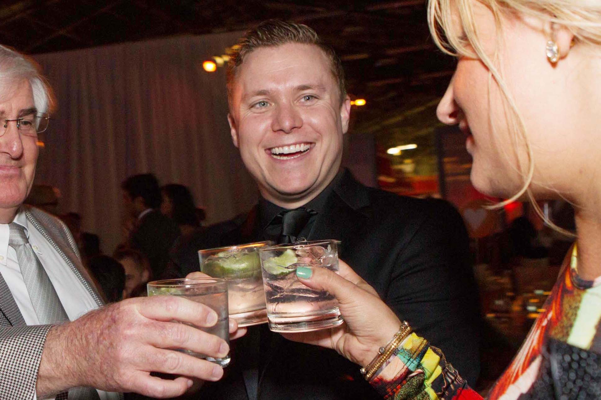 Three people holding drinks and cheers.