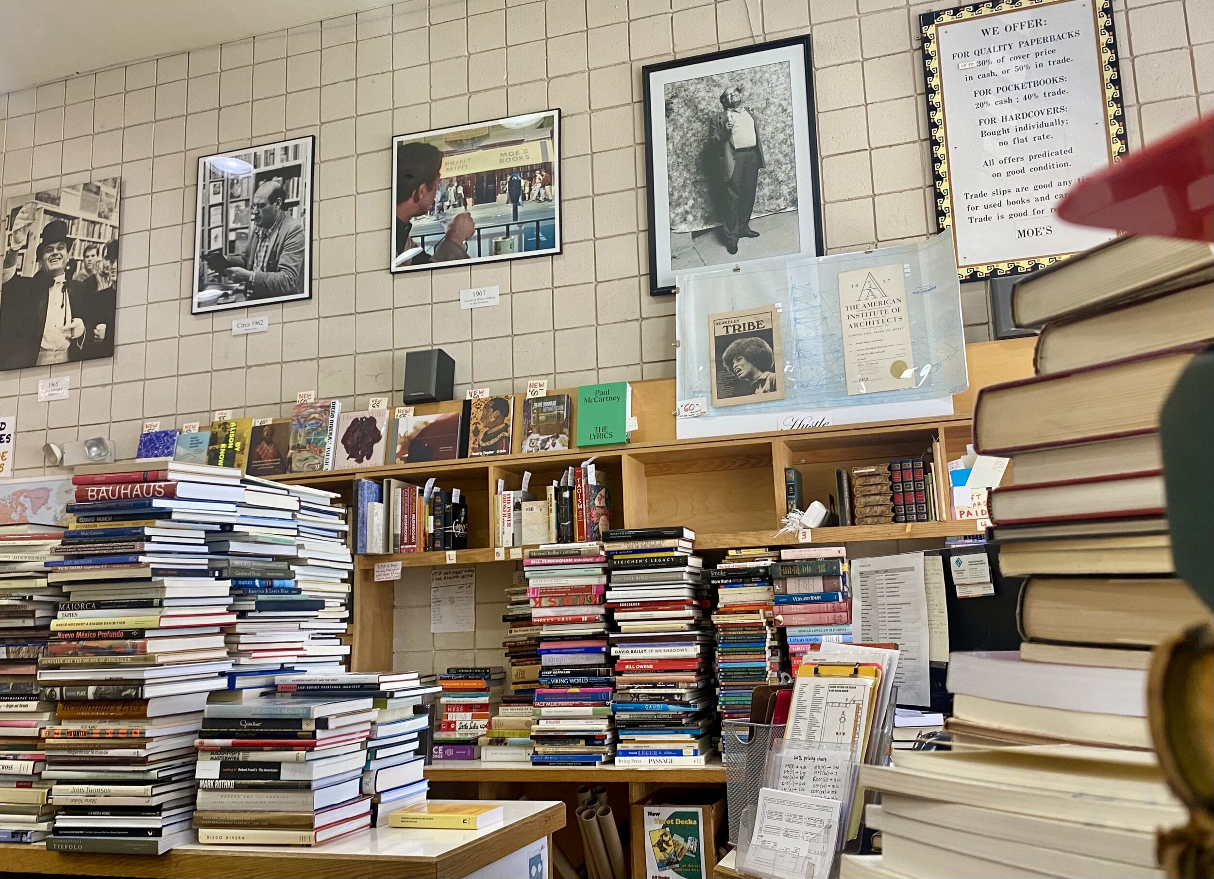 Stacks of books sit on tables with posters on the walls in the background.