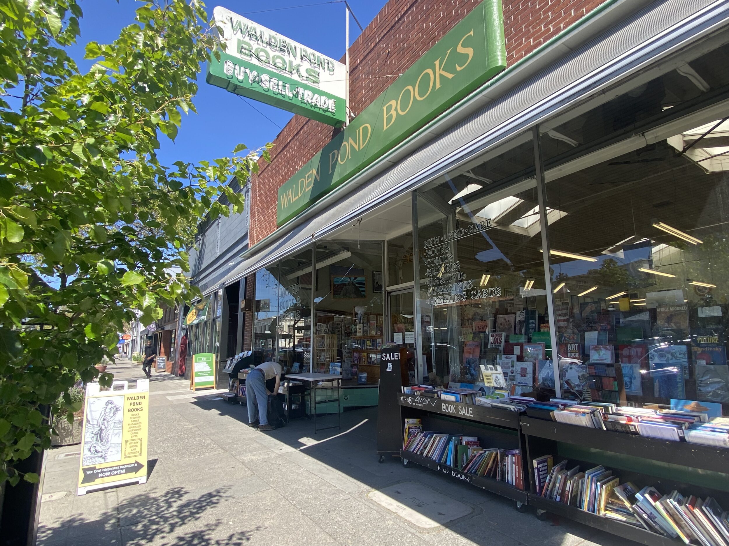 A building with an awning that says Walden Pond Books with tables stacked with books outside. 
