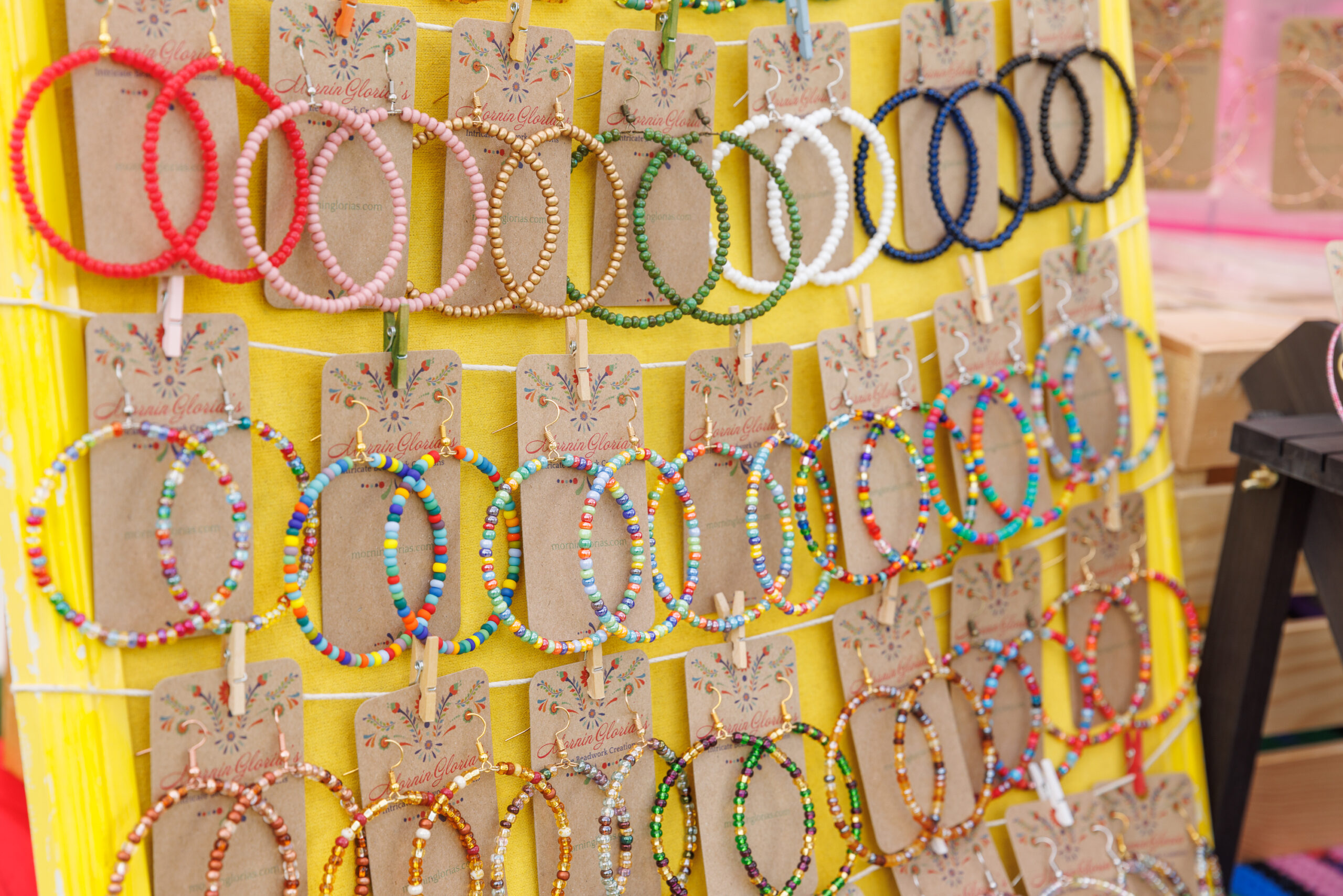 Colorful beaded hoop earrings displayed on a yellow stand with cardboard tags.