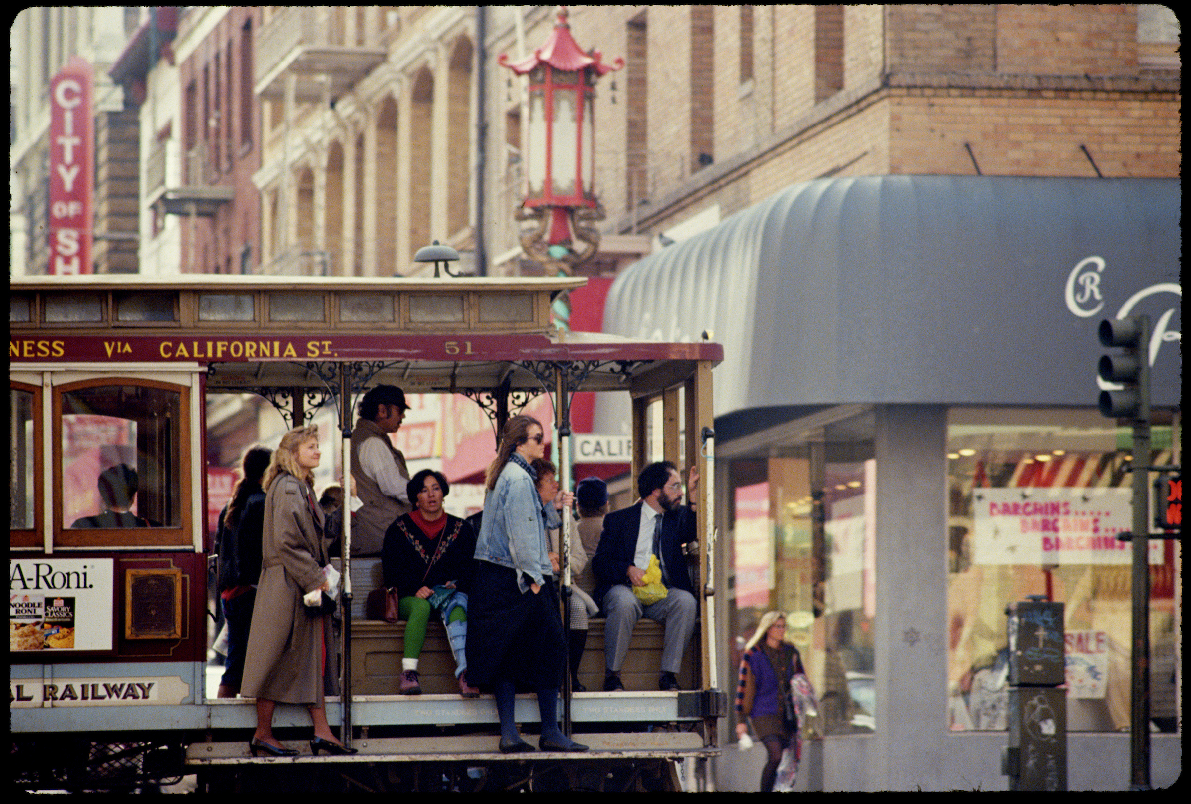 A picture shows a San Francisco street with a cable car going down it with people on the running boards.