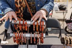 A person's hands touch bead bracelets displayed on a rack at an outdoor market.
