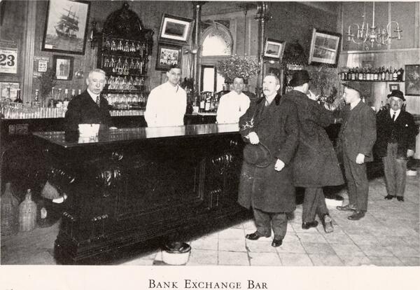 An old photograph of patrons and staff inside the Bank Exchange Bar, with a wooden bar and back shelves filled with bottles.