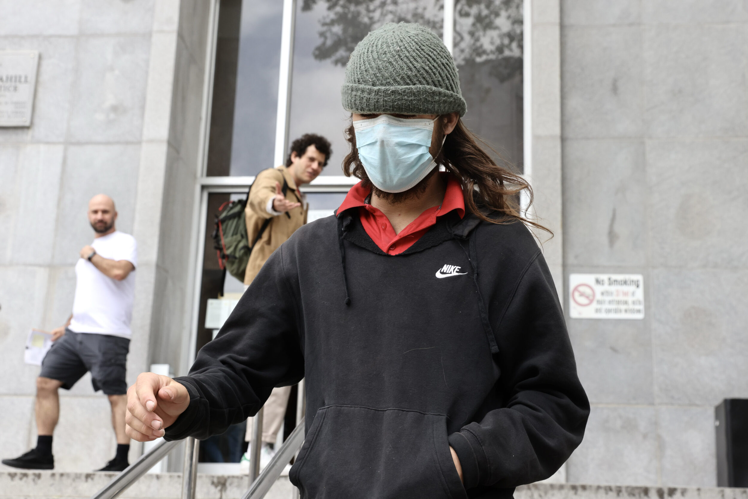 A person in a beanie and face mask descends steps, with onlookers in the background.